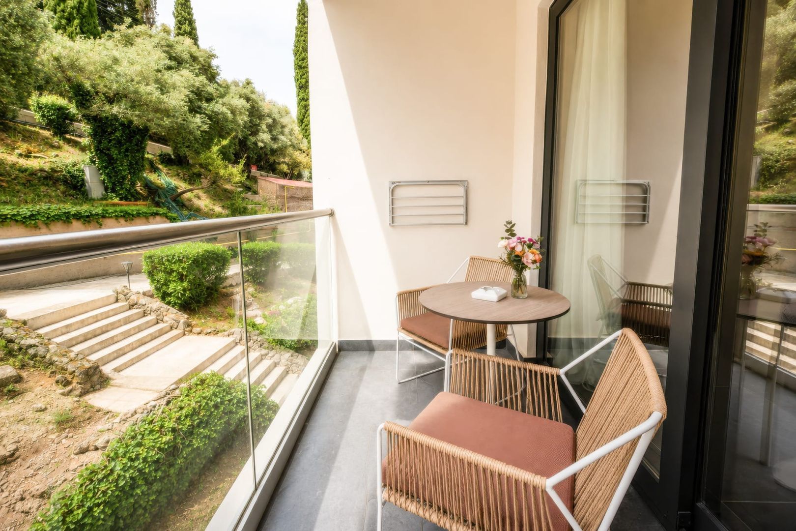 Hotelbalkon mit zwei modernen Stühlen, einem kleinen Tisch und Blick ins Grüne.