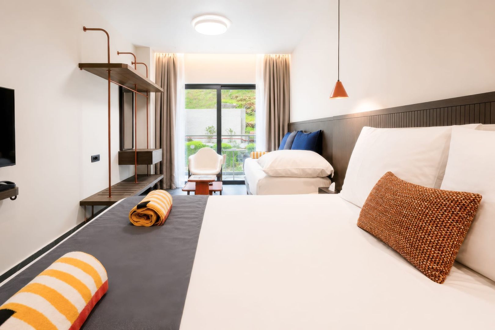 Modern eingerichtetes Hotelzimmer mit Doppelbett, Tagesbett und Zugang zum Balkon.