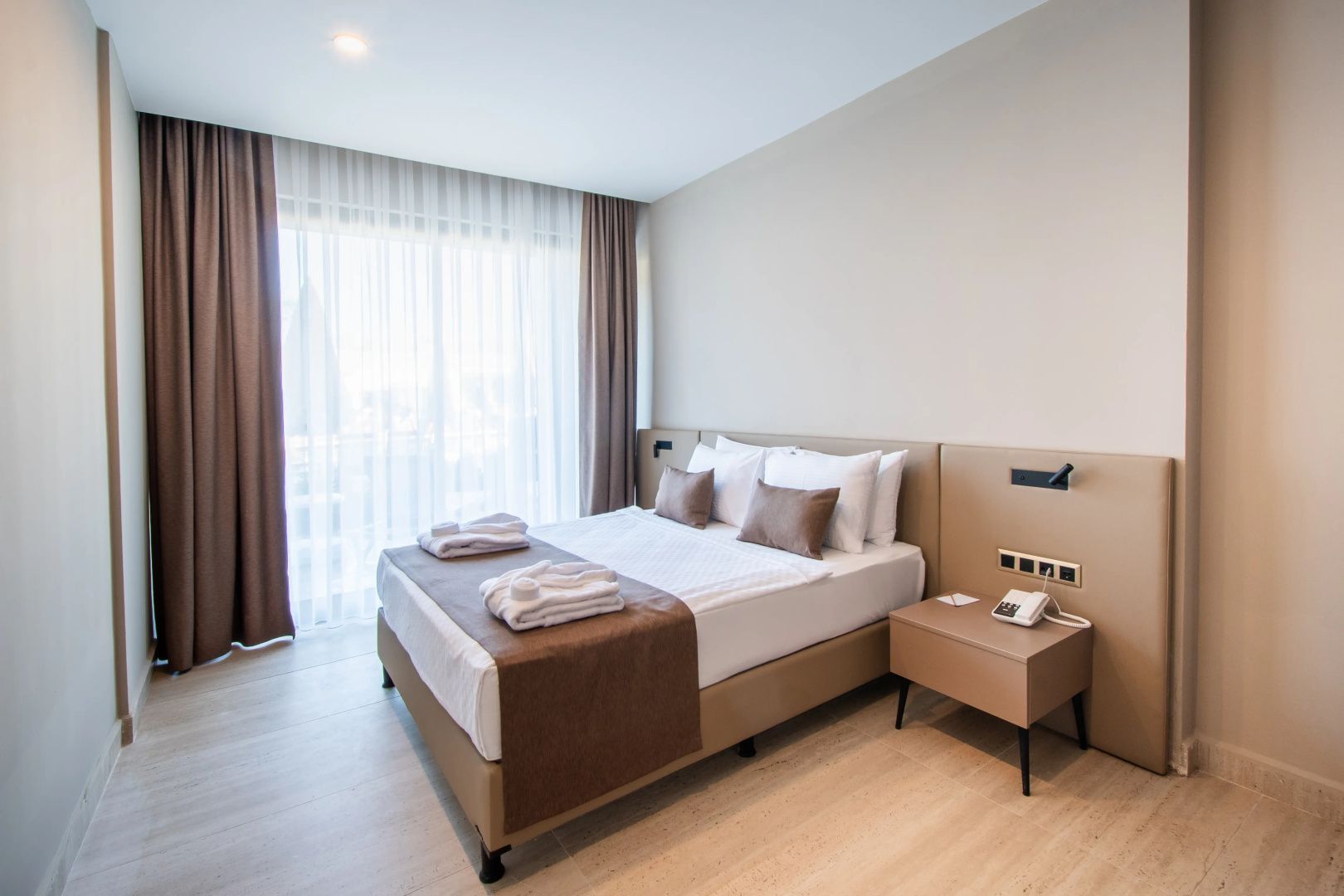Doppelbett mit weißer Bettwäsche, brauner Tagesdecke und einem Beistelltisch im Hotelzimmer.