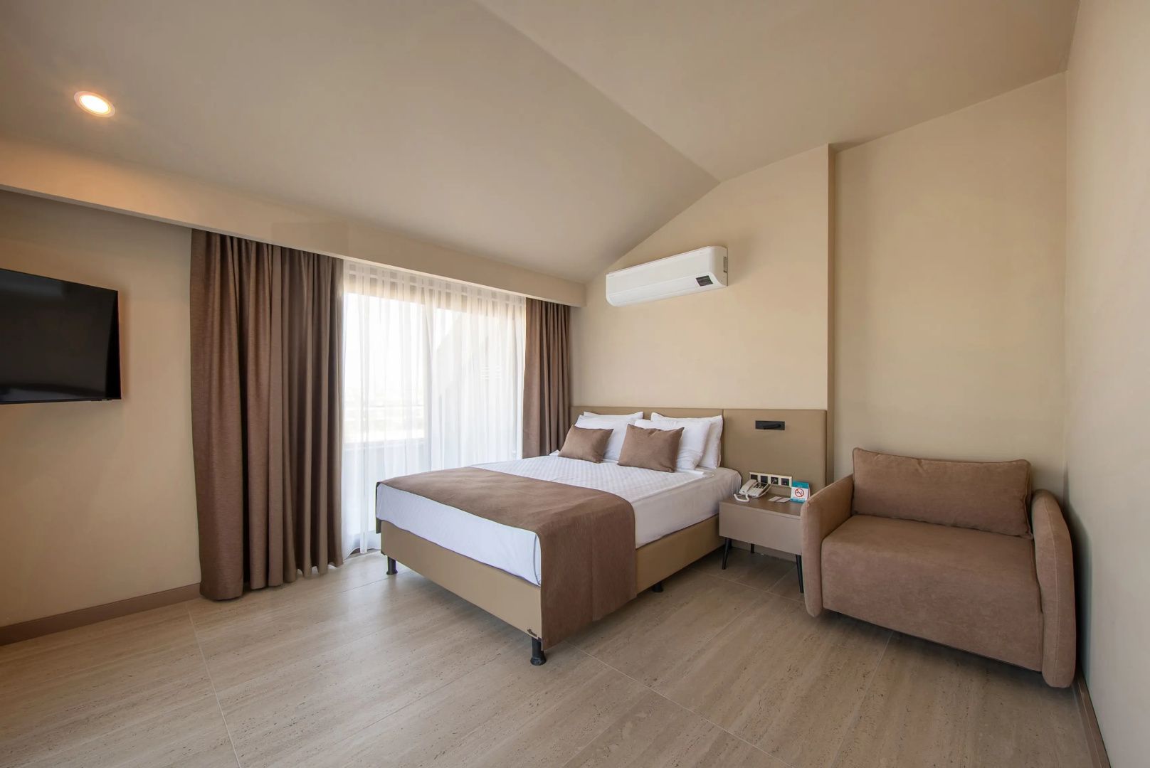 Schlafzimmer mit Doppelbett, Sessel, Klimaanlage und Vorhängen.