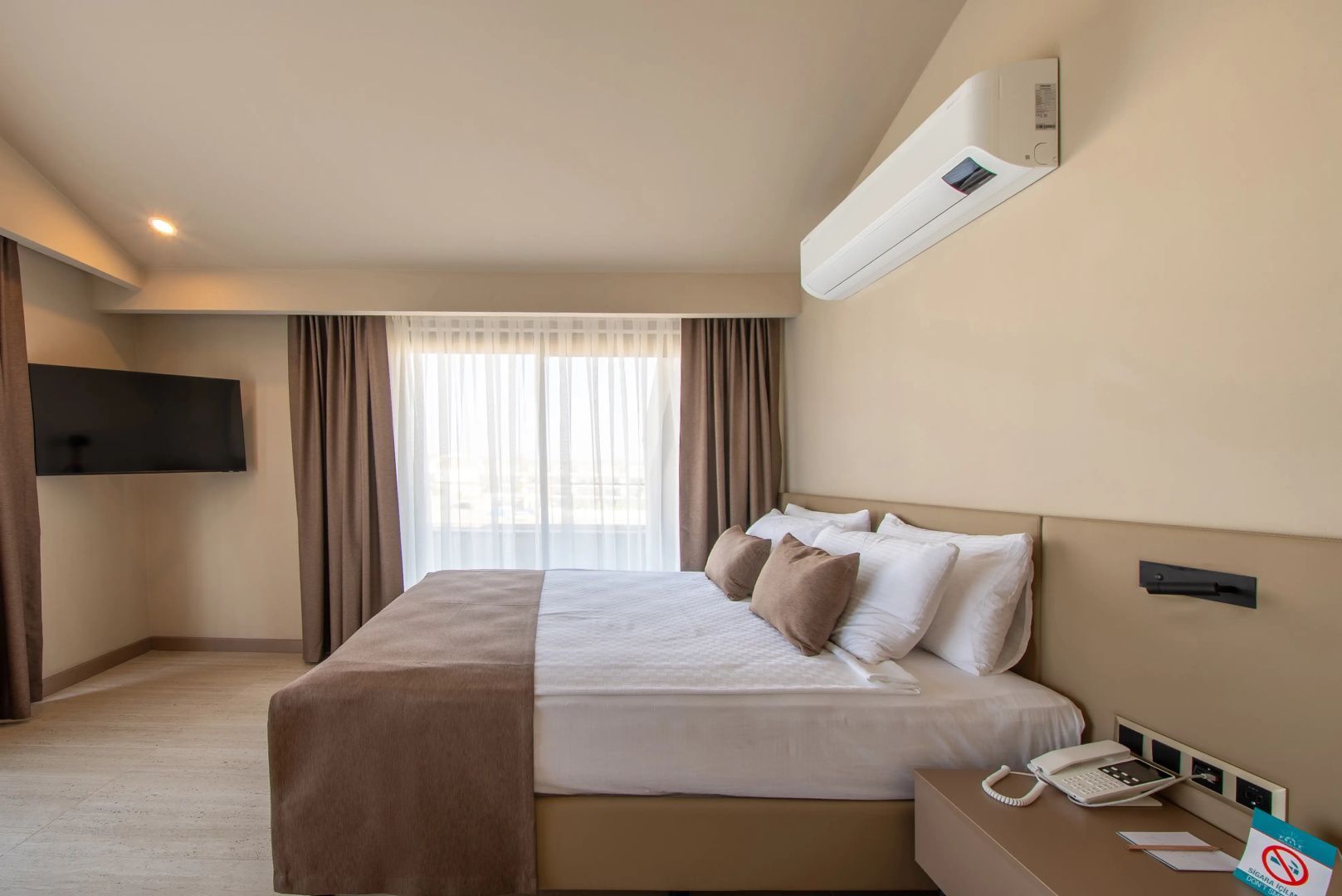 Doppelbett mit braunen Kissen, Nachttisch und Klimaanlage an der Wand im Hotelzimmer.