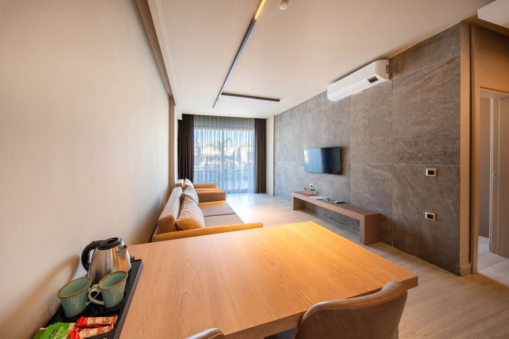 Wohnzimmer einer Suite mit Fernseher an der Steinwand, Sofa und Holztisch mit Wasserkocher.