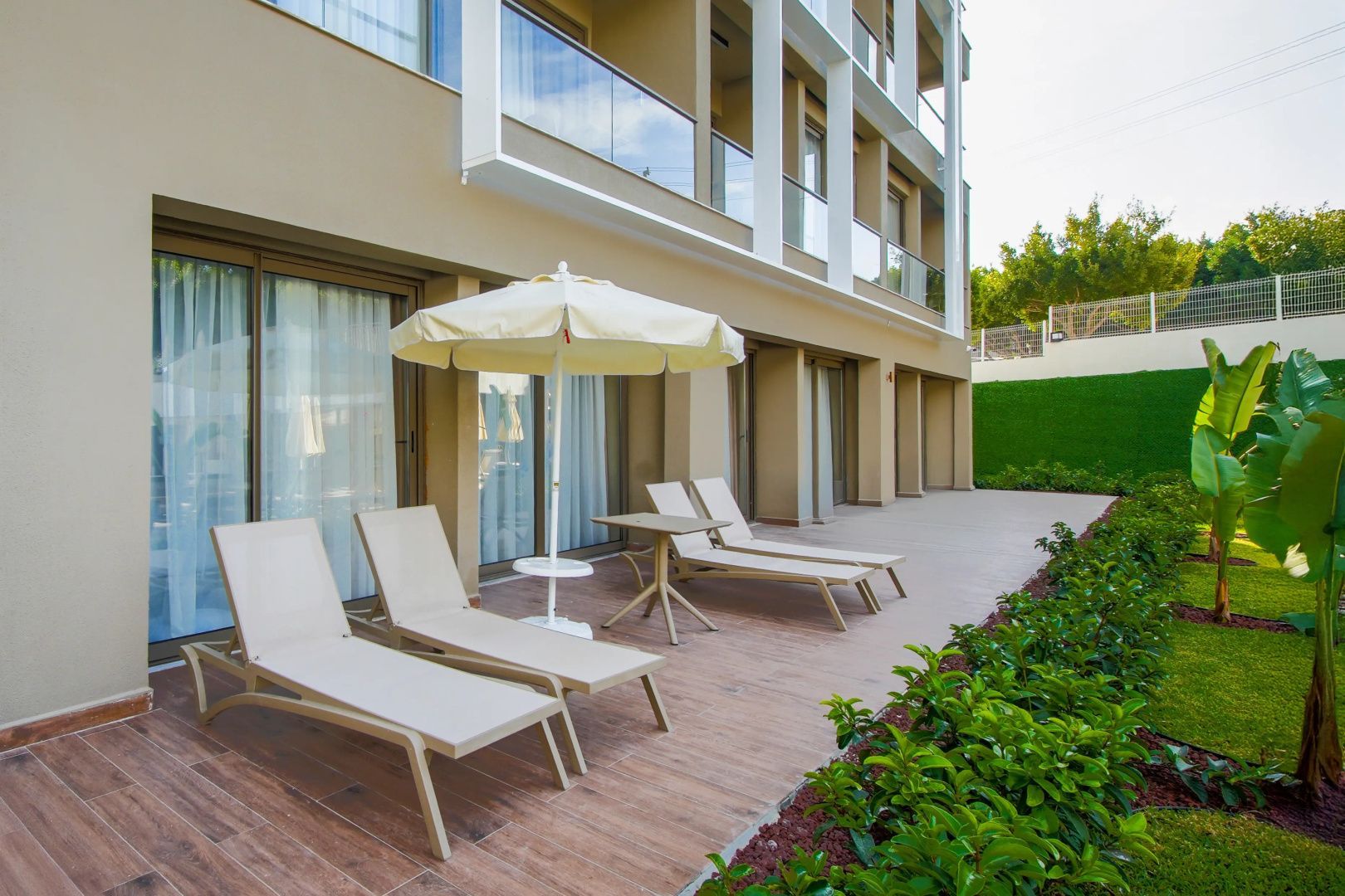 Terrasse im Erdgeschoss mit zwei Sonnenliegen, Sonnenschirm und Hotelfassade.