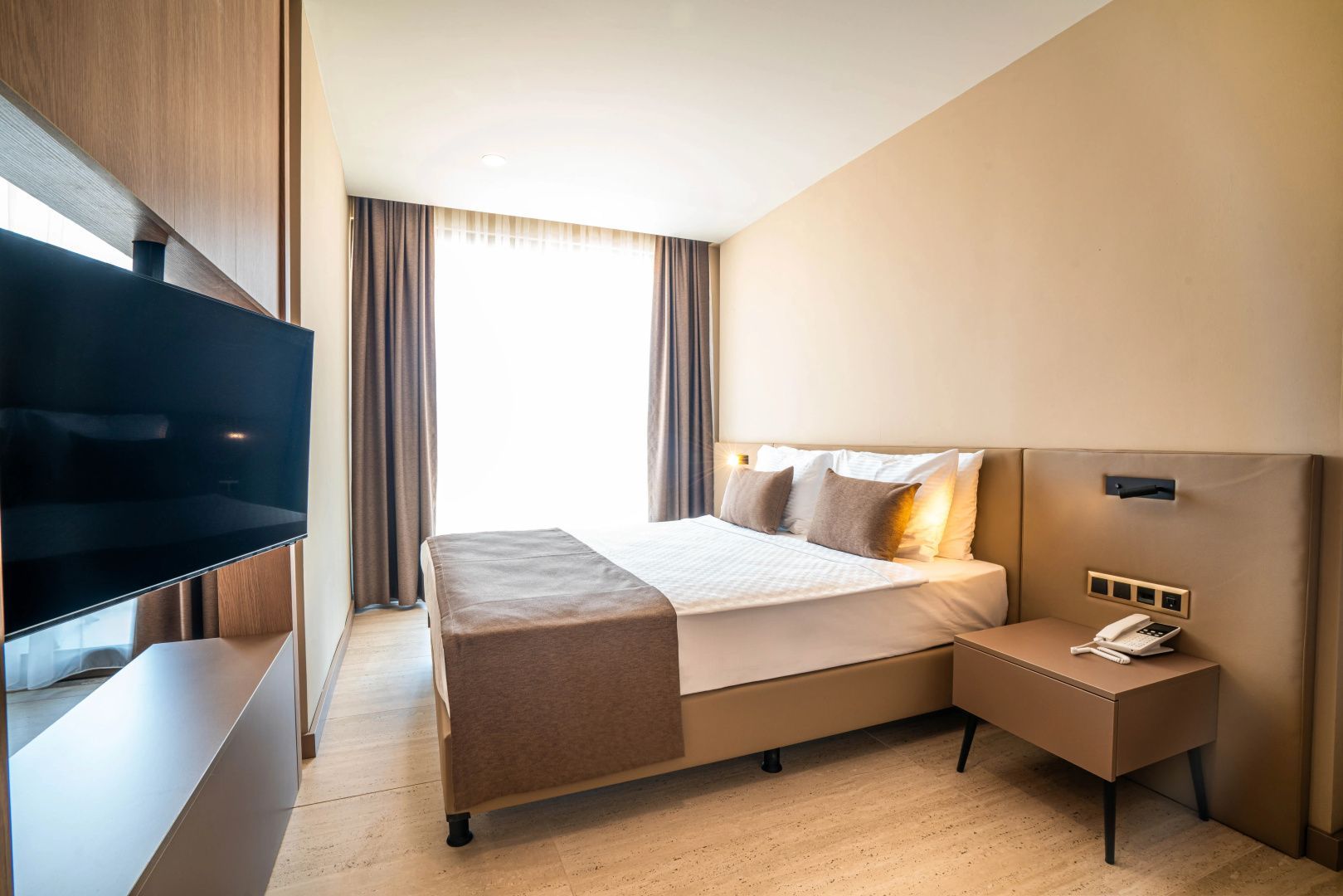 Modernes Hotelzimmer mit Doppelbett, Nachttisch und wandmontiertem Fernseher.