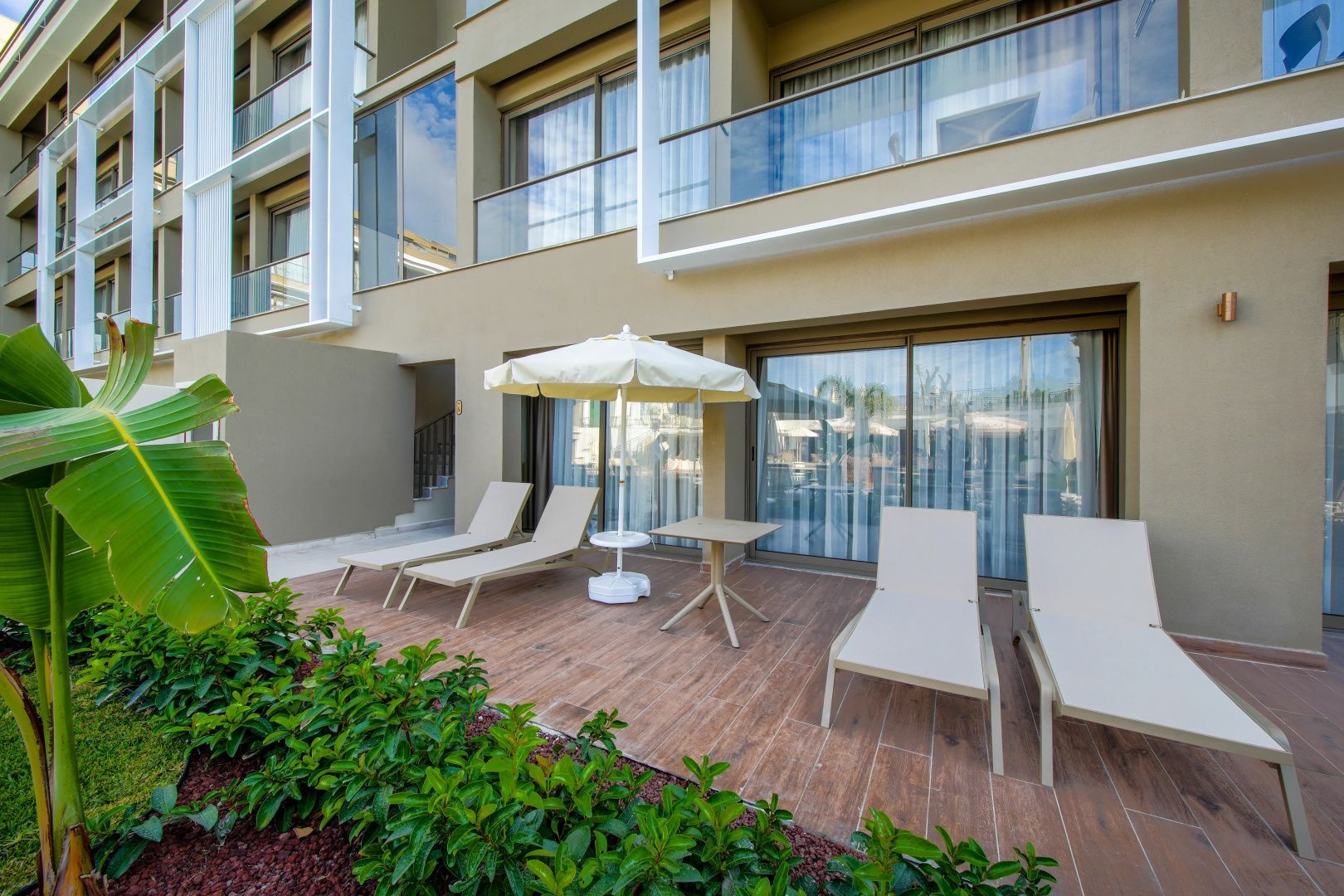 Terrasse im Erdgeschoss mit mehreren Liegestühlen, Sonnenschirm und Glastüren zur Unterkunft.