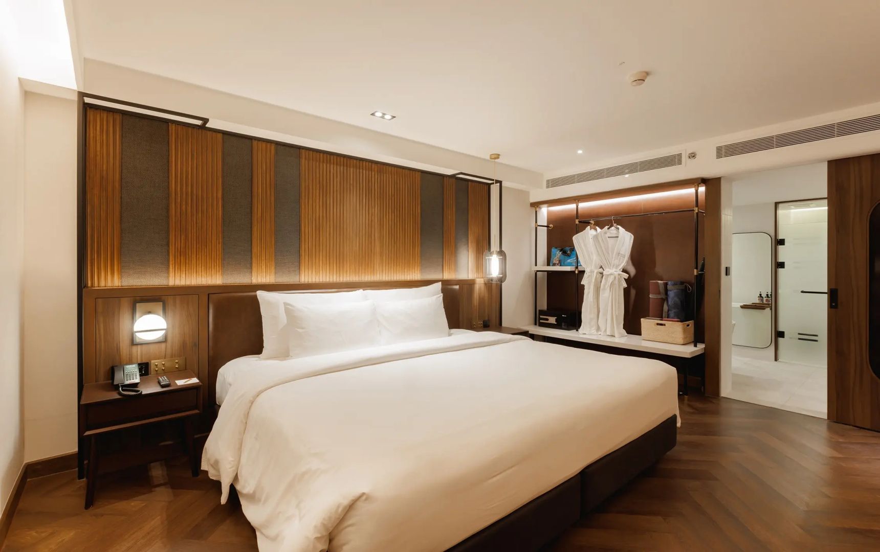 Großes Doppelbett mit weißer Bettwäsche und eine offene Garderobe mit Bademänteln.