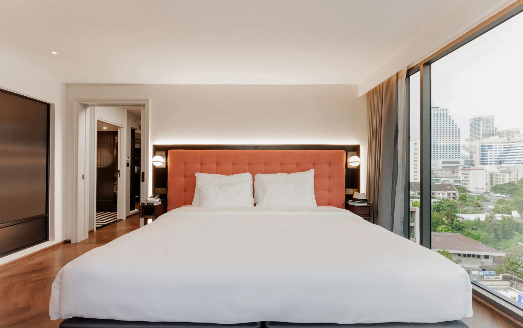 Doppelbett mit weißer Bettwäsche und lachsfarbenem Kopfteil in einem Hotelzimmer