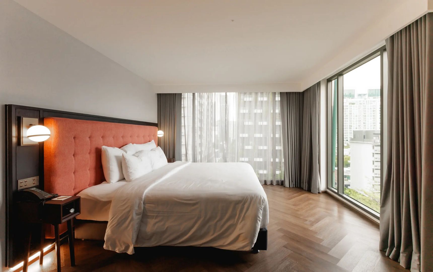 Hotelzimmer mit großem Bett, Holzboden und bodentiefen Fensterfronten.