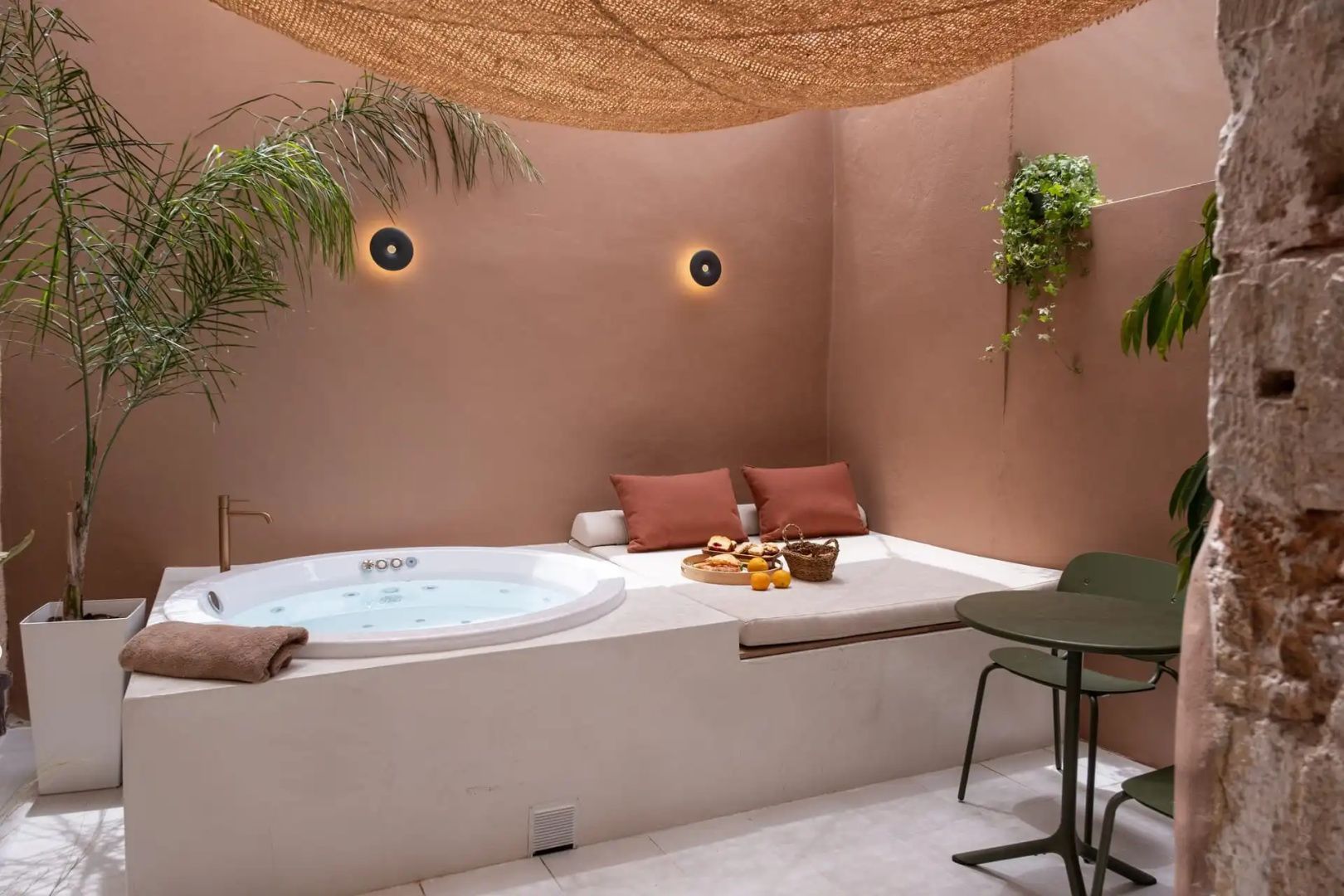Private Terrasse mit rundem Whirlpool, Tagesbett und Wandleuchten unter einem Sonnensegel.