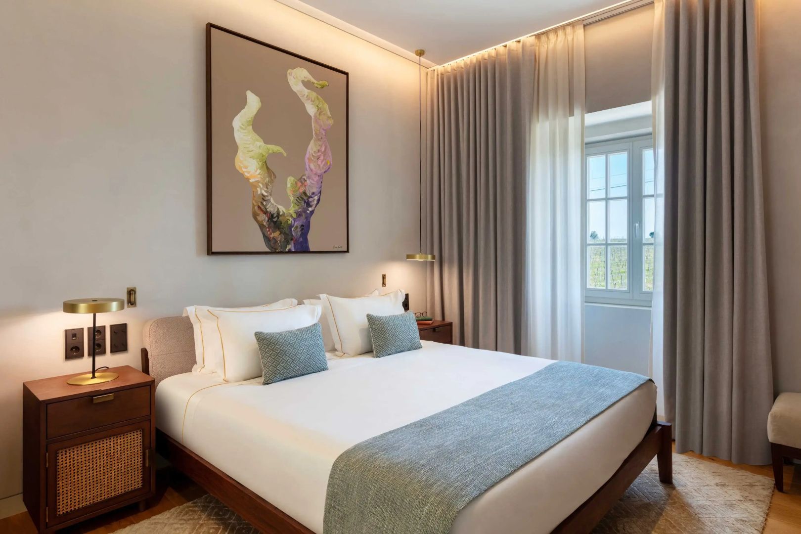 Doppelbett mit weißer Bettwäsche, Kunstwerk an der Wand und Vorhängen neben dem Fenster.