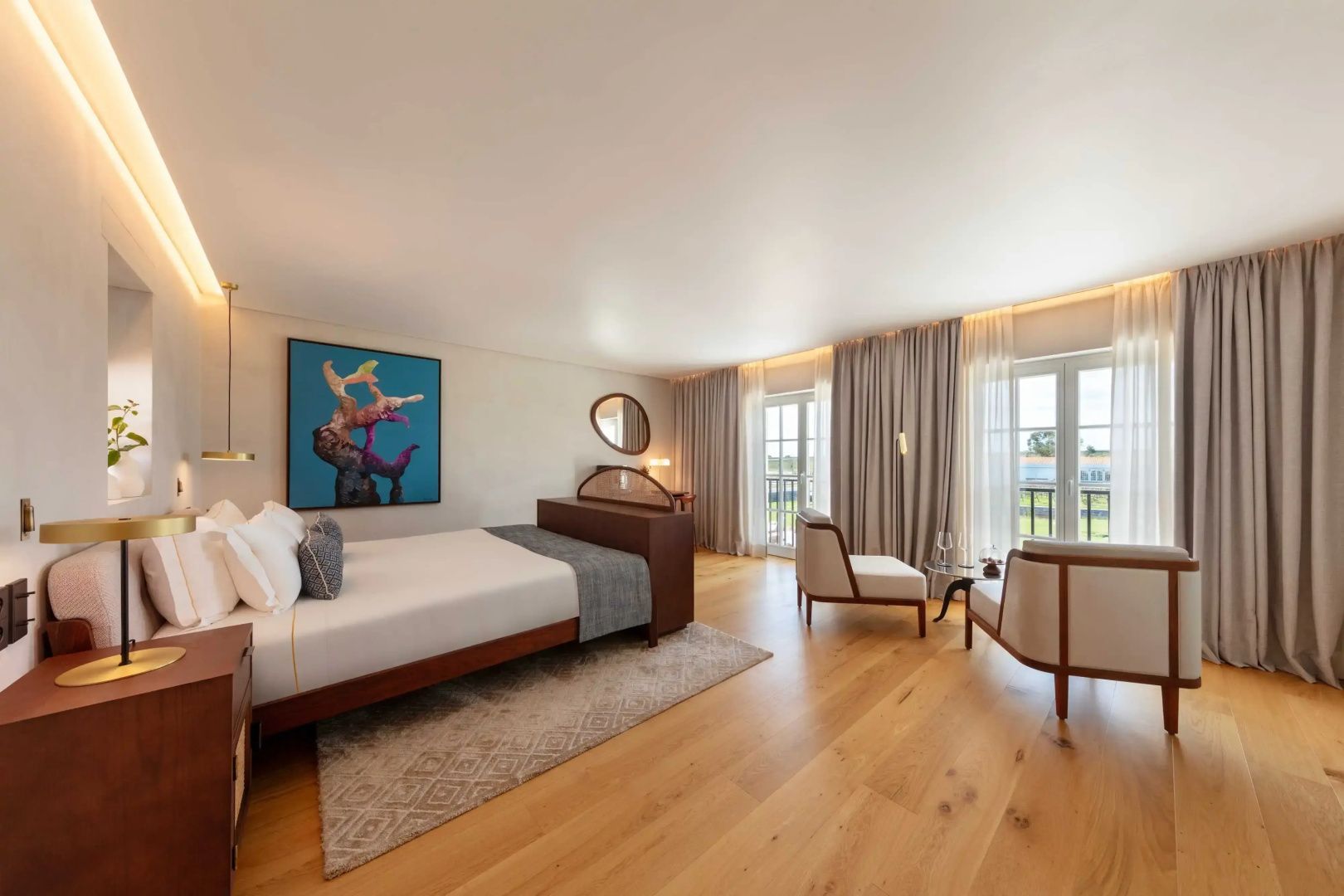 Schlafzimmer mit Doppelbett, Sitzbereich mit zwei Sesseln und großen Fensterfronten ins Freie.
