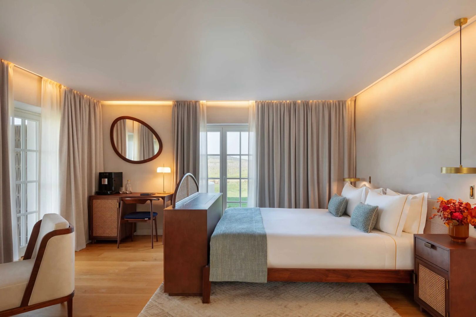 Hotelzimmer mit Holzboden, einem Doppelbett, Schreibtisch und großer Fenstertür.