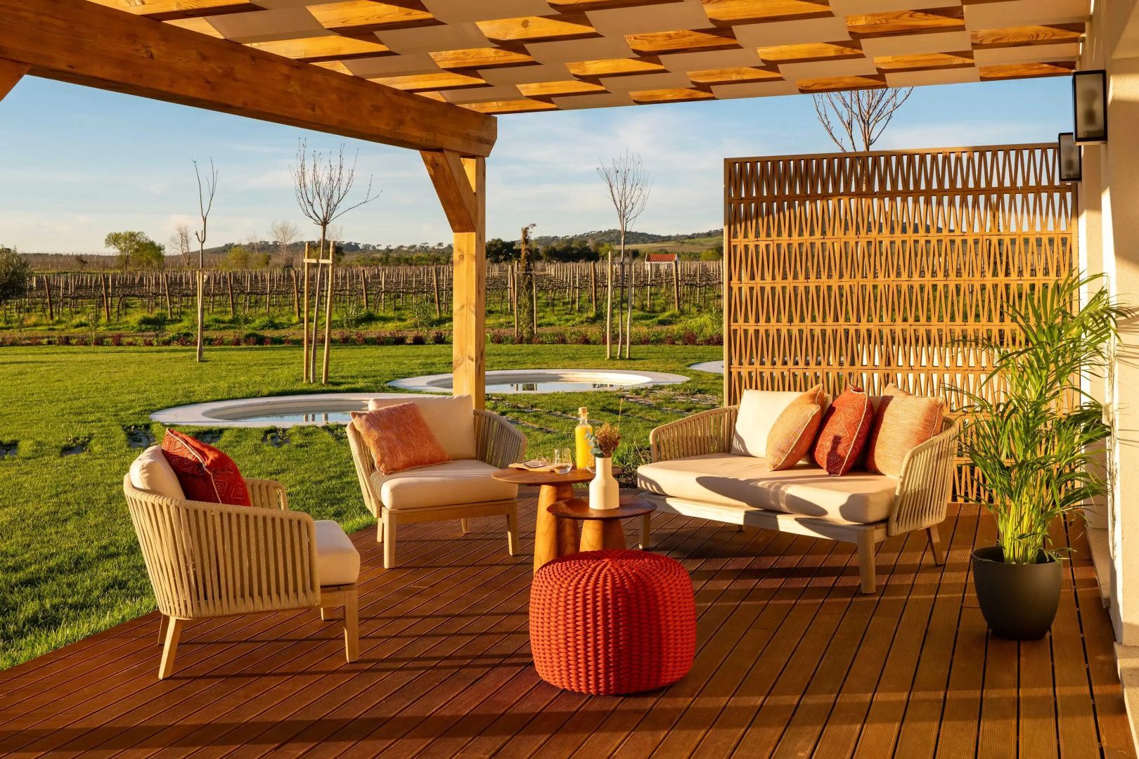 Möblierte Holzterrasse unter einer Pergola mit Blick auf Weinberge und Natur.