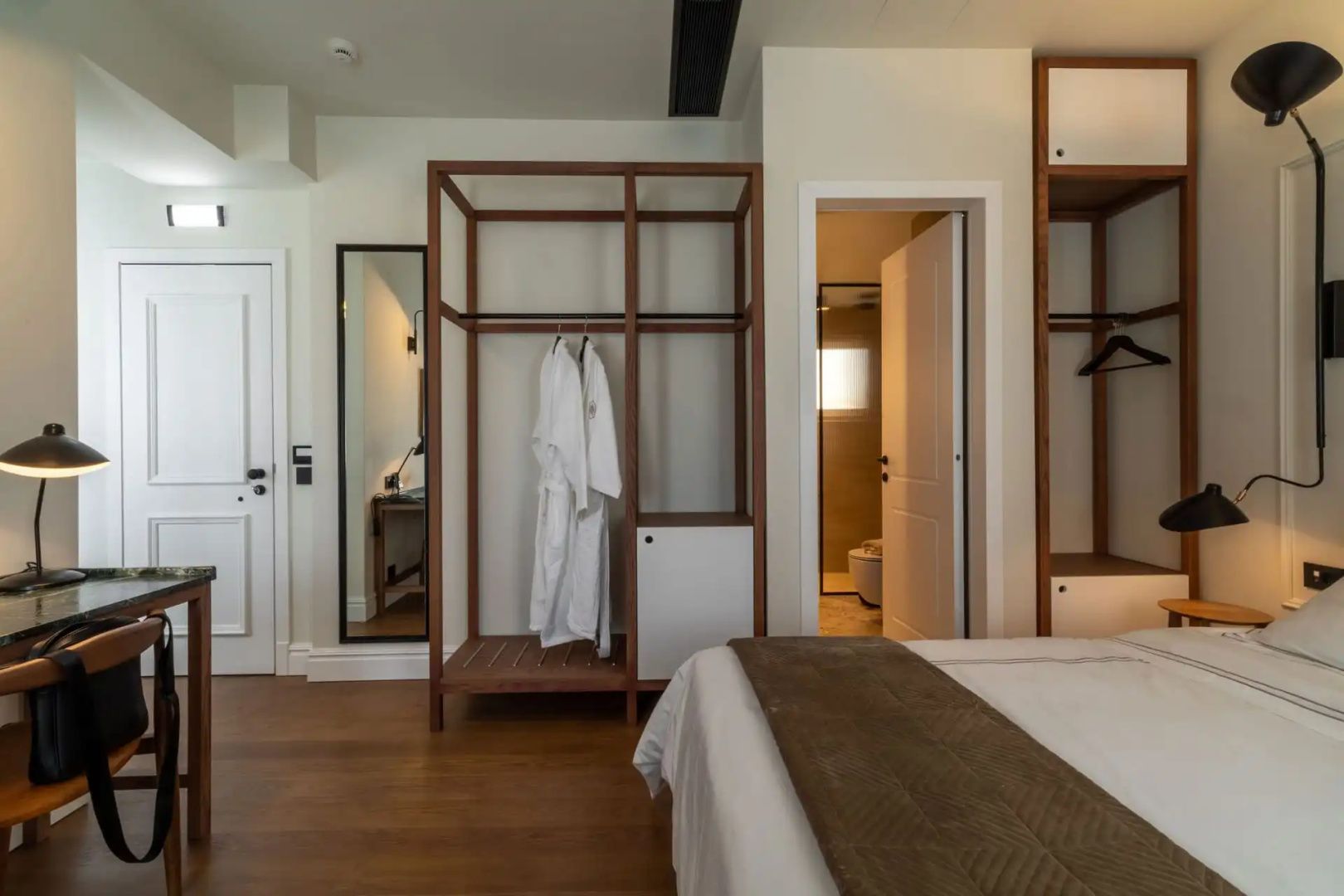 Offener Holzkleiderschrank mit Bademänteln und Blick in das angrenzende Badezimmer.