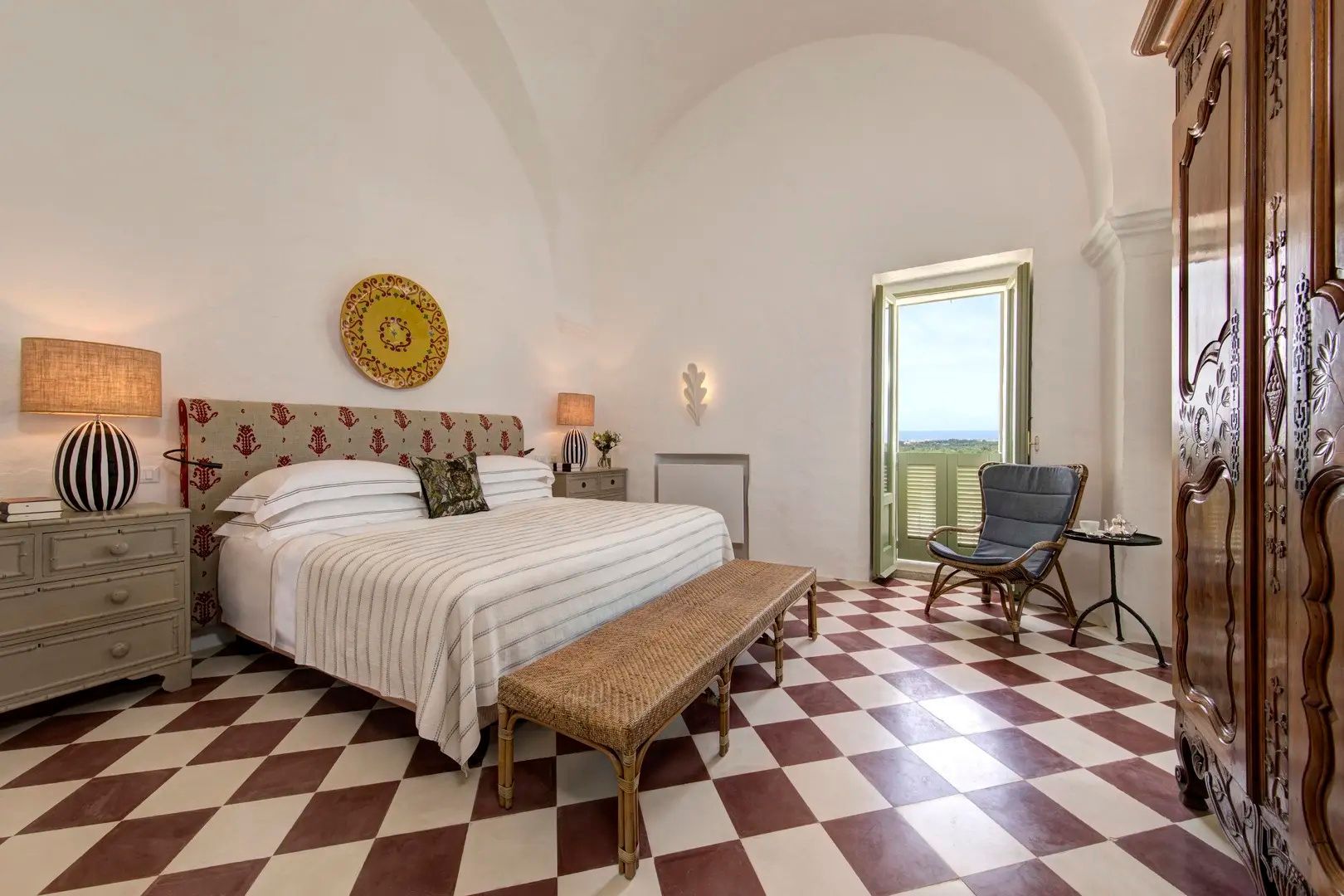 Helles Hotelzimmer mit Doppelbett, getöntem Fliesenboden, Sessel und Blick ins Freie.