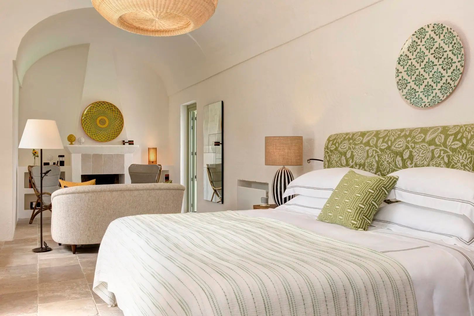 Helles Hotelzimmer mit Doppelbett, grünem Kopfteil, Nachttischlampe und Kamin im Hintergrund.