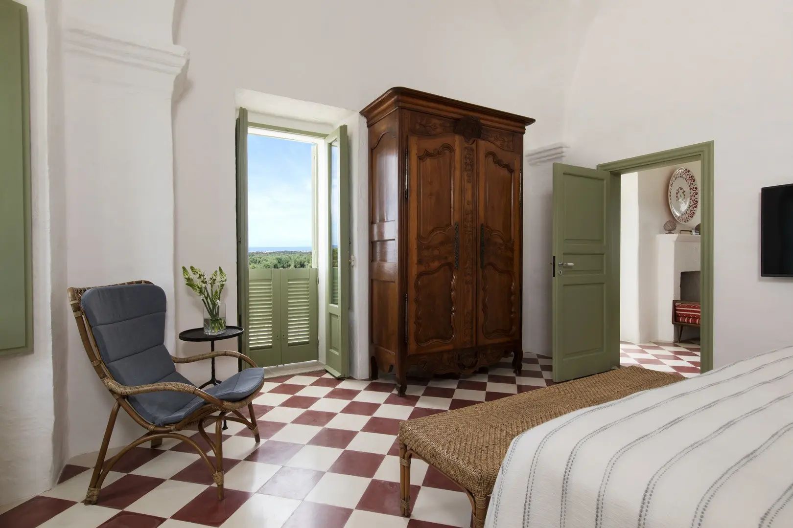 Hotelzimmer mit Antik-Holzschrank, Sessel und geöffneter Balkontür mit Blick aufs Meer.