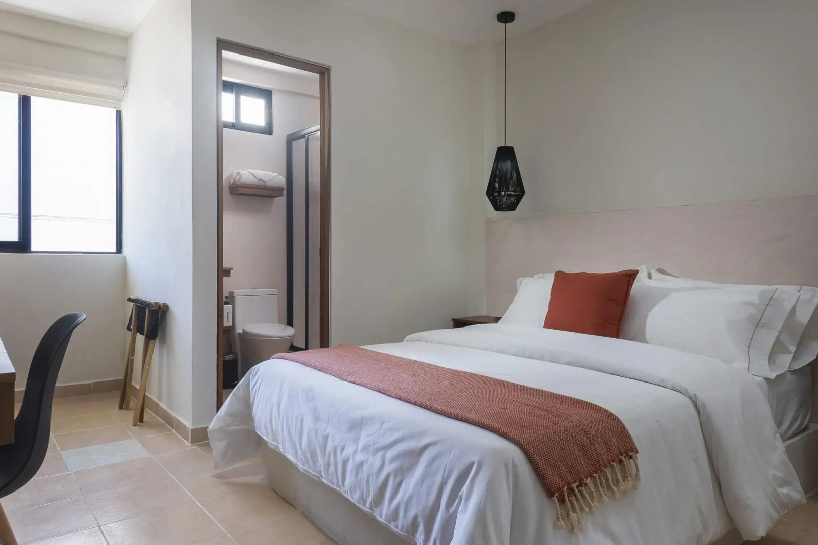 Helles Hotelzimmer mit Doppelbett, weißer Bettwäsche und Durchgang zum Badezimmer.
