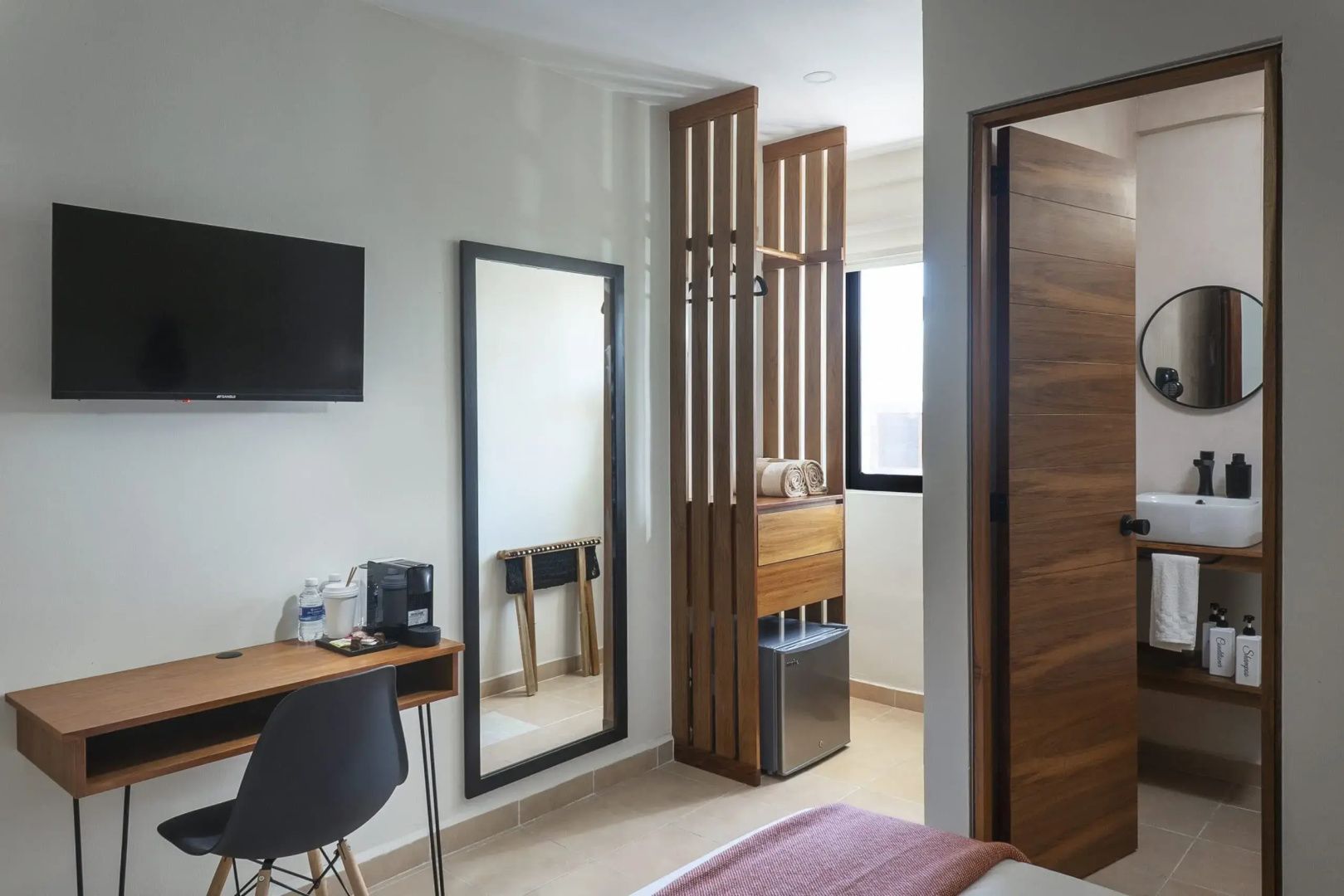 Moderne Zimmerausstattung mit Raumteiler aus Holz, Minibar und Wandspiegel.