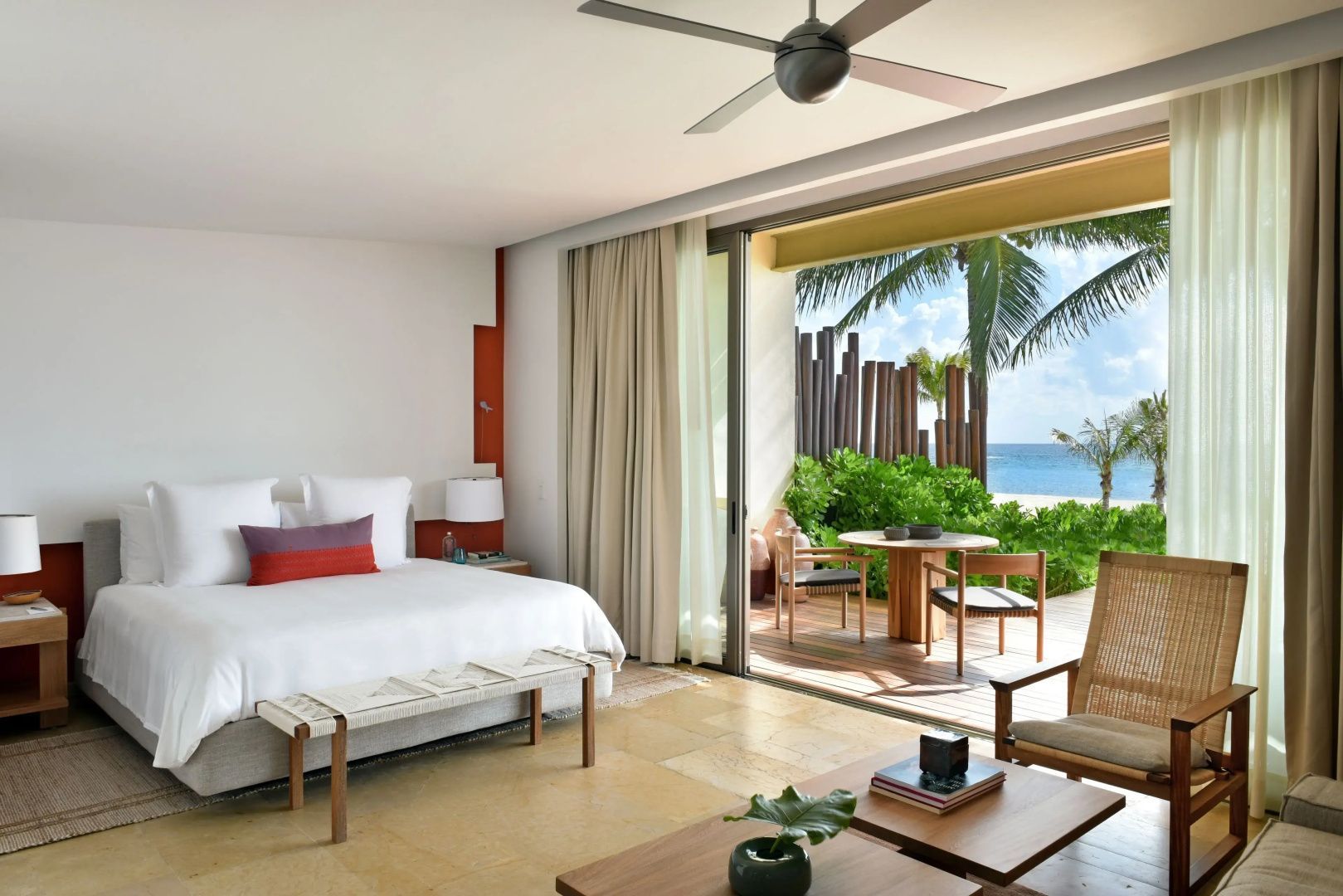 Helles Schlafzimmer mit Doppelbett, Sitzbereich und offenen Glastüren zur Terrasse am Meer.