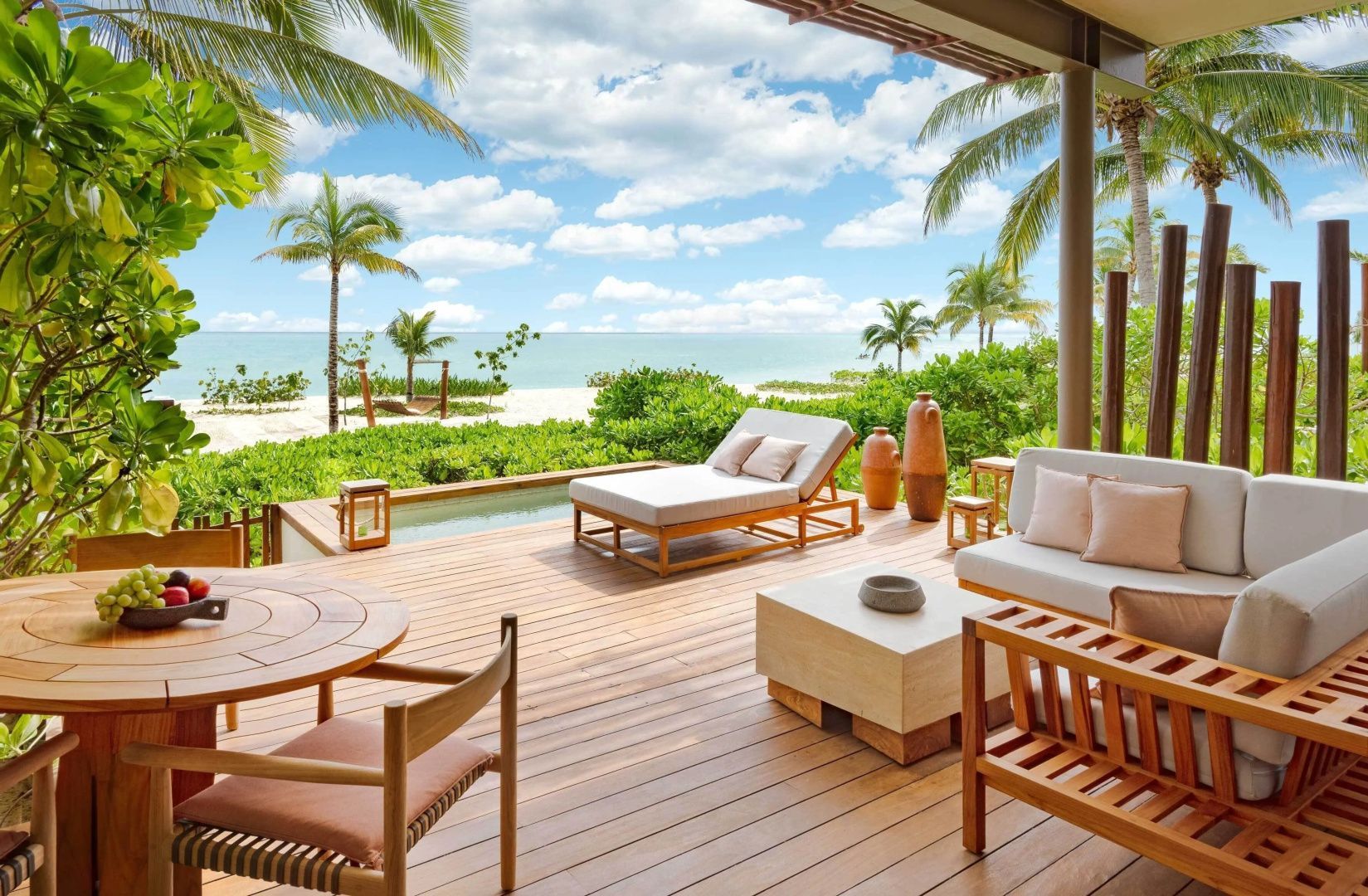 Holzterrasse mit Sonnenliege, Sitzmöbeln und kleinem Pool mit Blick auf Strand und Meer.