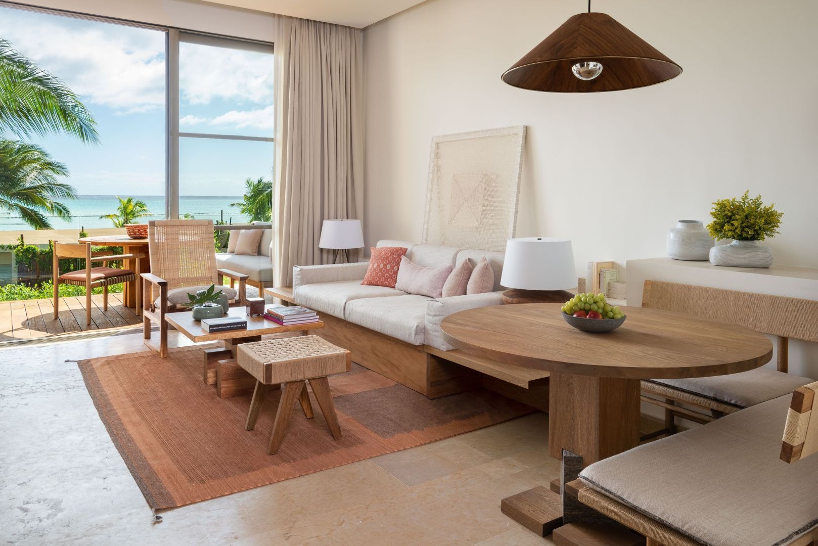 Helles Wohnzimmer mit weißer Couch, Holztisch und großem Fenster mit Blick auf das Meer.