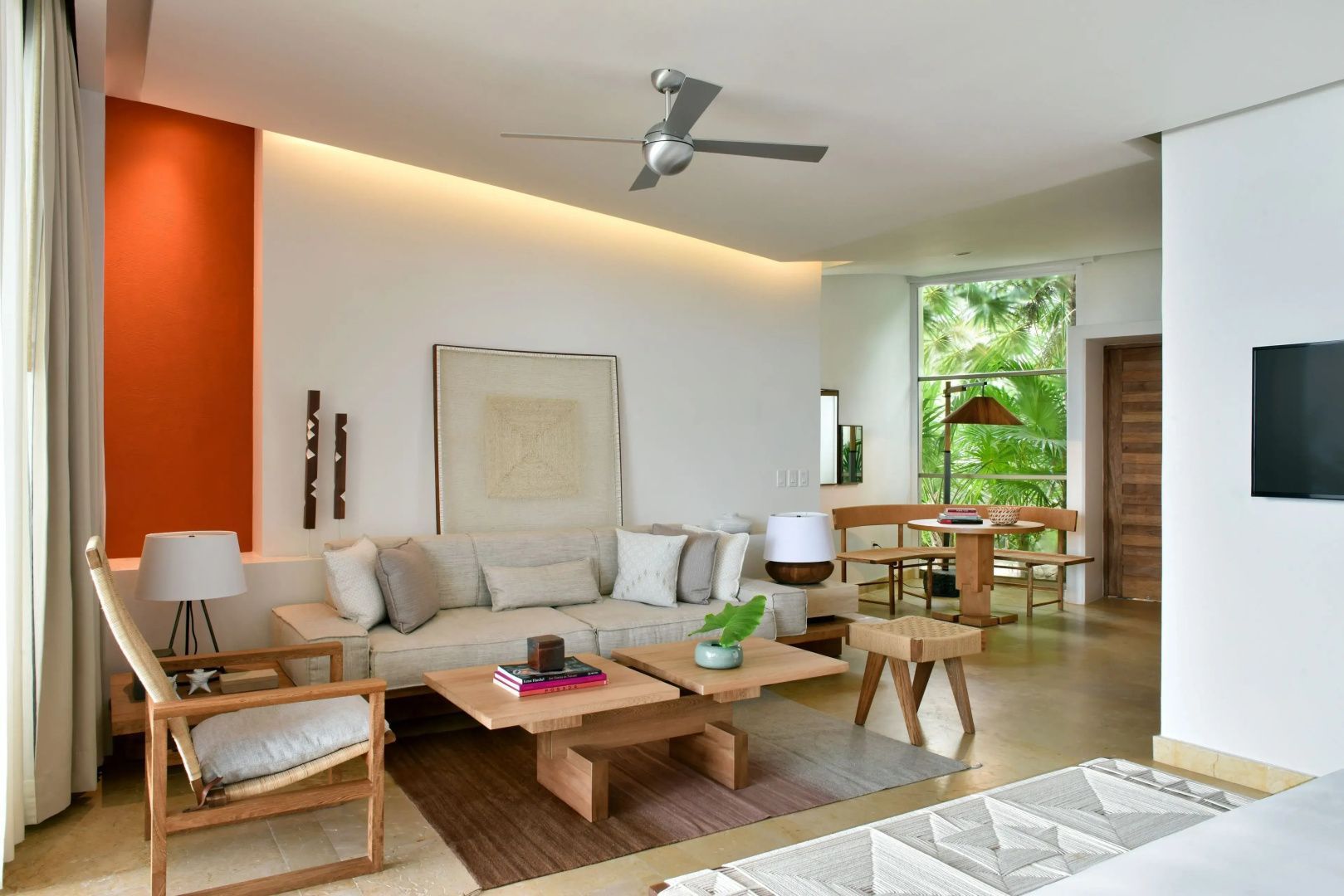 Wohnbereich mit hellem Sofa, Holztischen, Deckenventilator und Essbereich im Hintergrund.