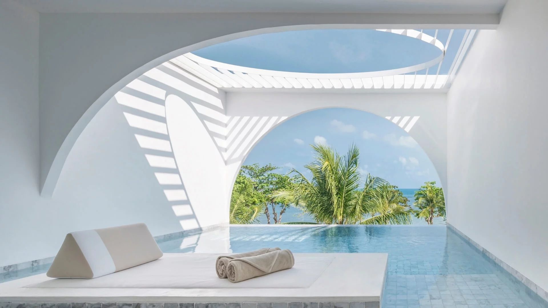 Überdachter Poolbereich einer Terrasse mit Blick auf grüne Palmen und das blaue Meer.