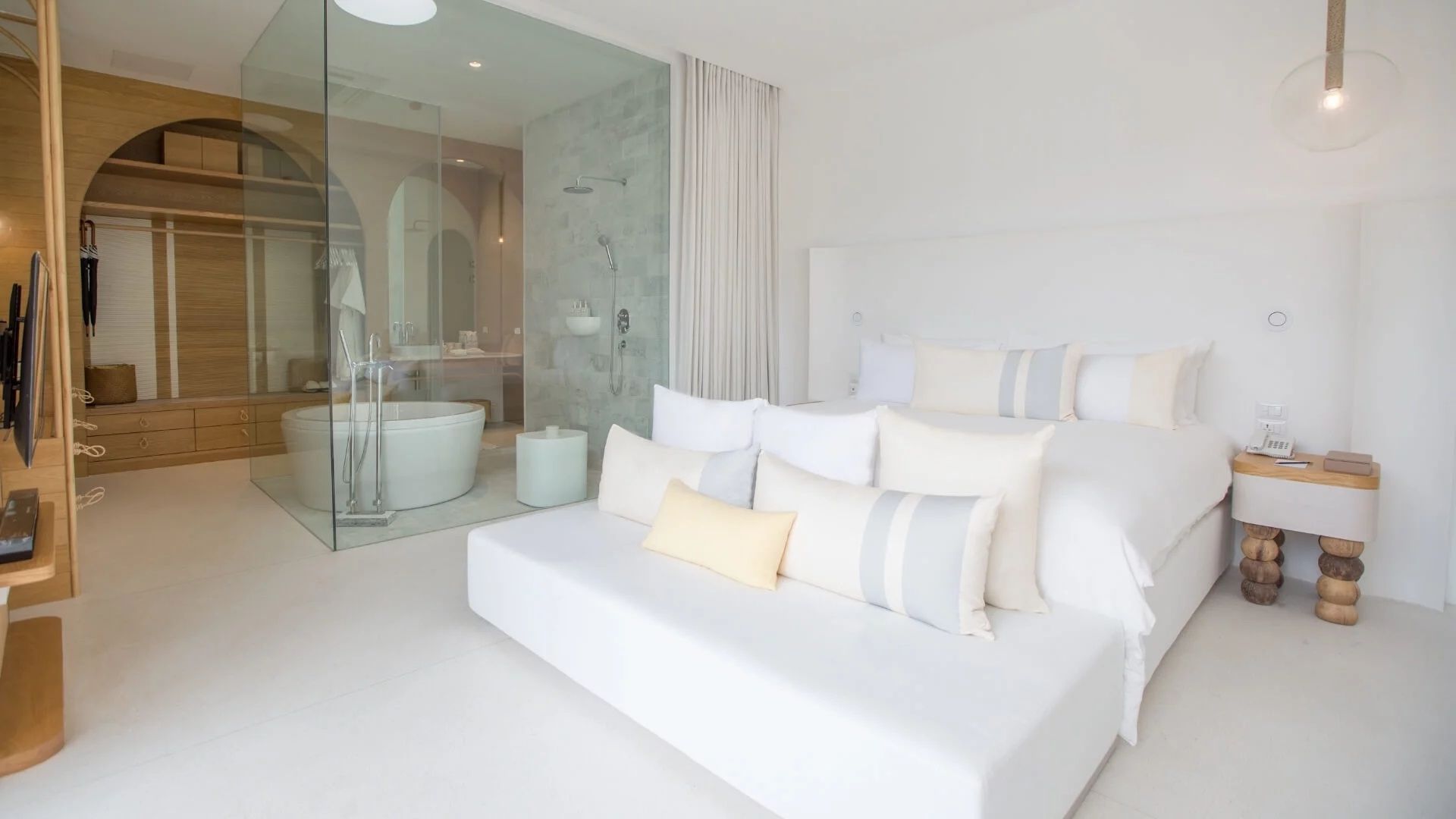 Helles Hotelzimmer mit großem Doppelbett, Kissen und angrenzendem verglastem Badezimmer.