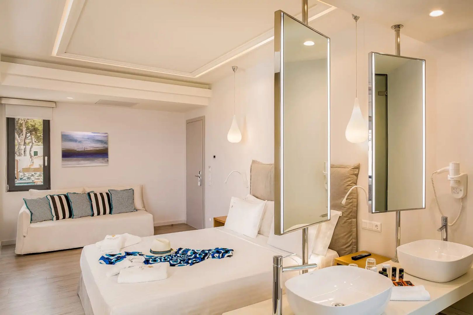 Moderne Suite mit Doppelbett, Waschtisch im Raum und hellem Sofa im Hintergrund.