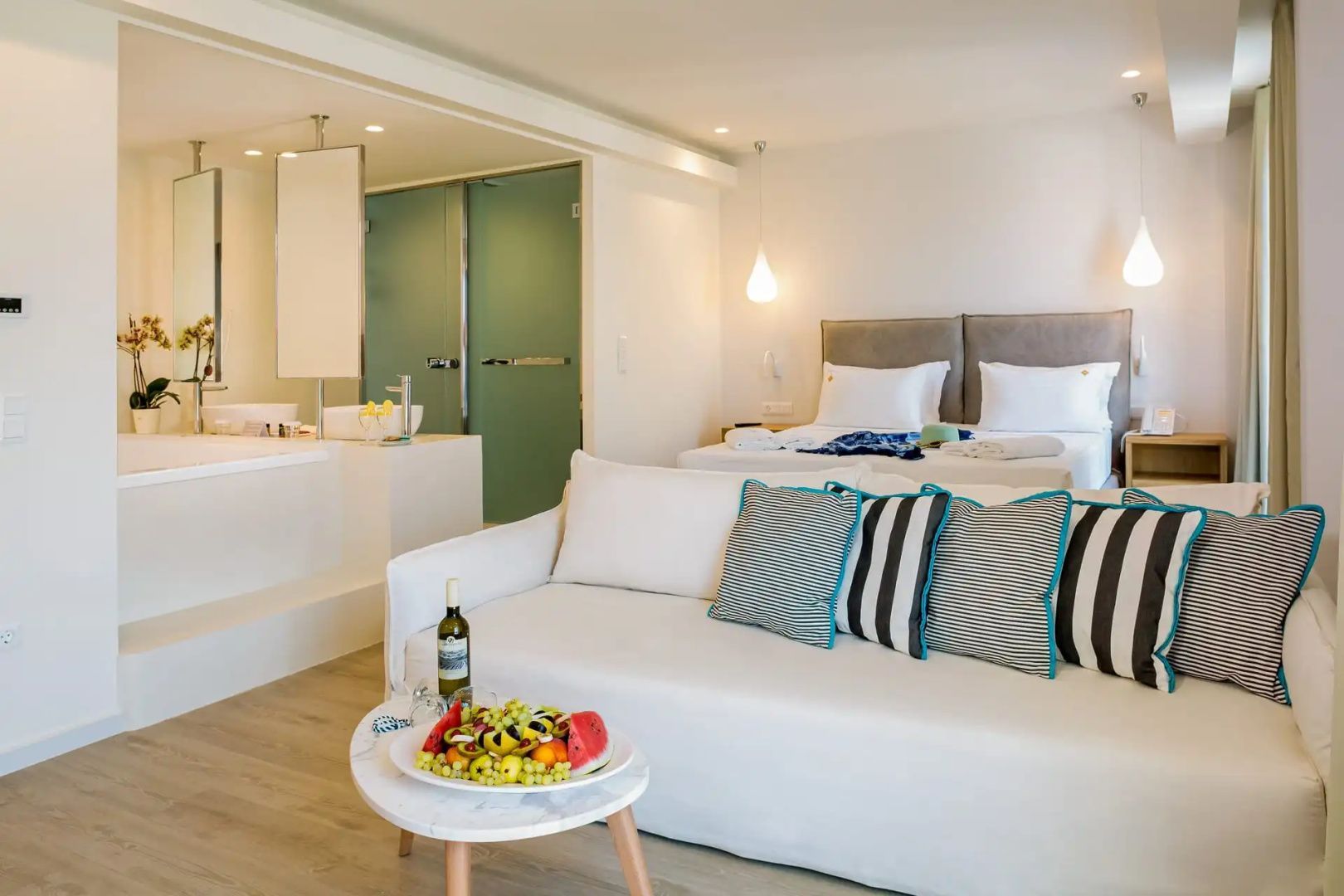 Hell eingerichtete Suite mit weißem Sofa, Beistelltisch, Doppelbett und Badbereich.