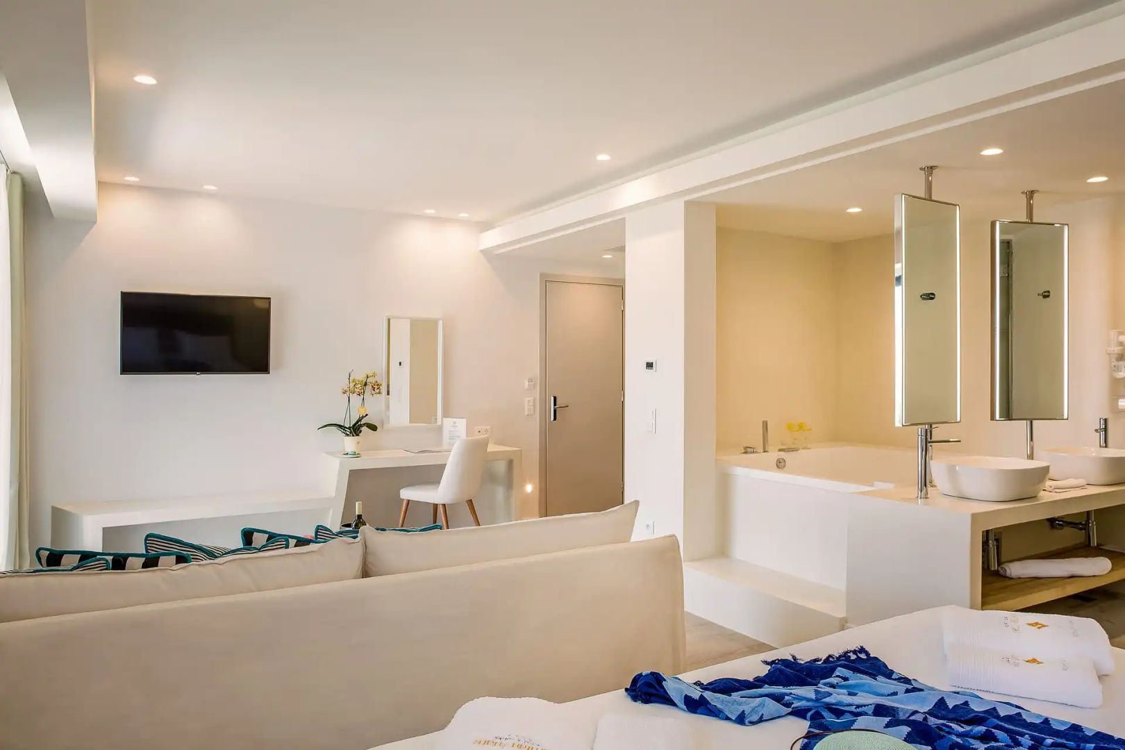Großzügiges Zimmer mit weißem Sofa, Schreibtisch, Wandfernseher und integriertem Whirlpool.