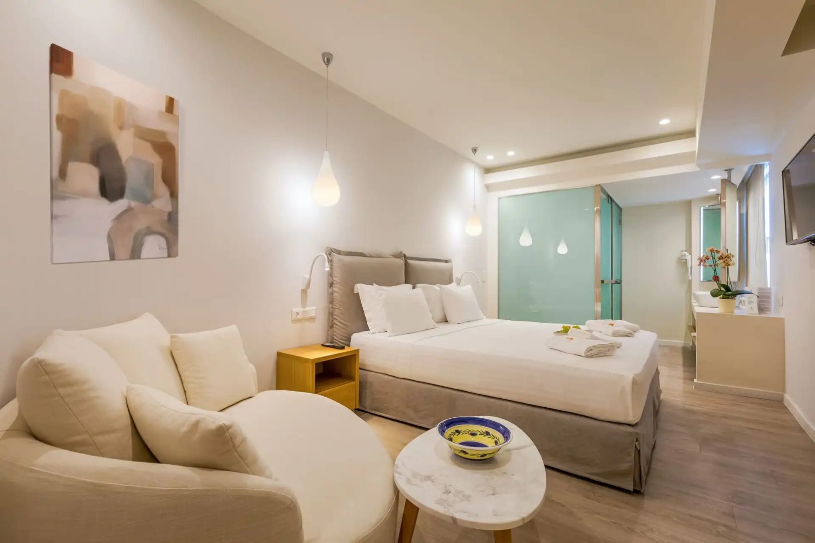 Hotelzimmer mit großem Doppelbett, Pendelleuchten und hellem Sessel im Vordergrund.