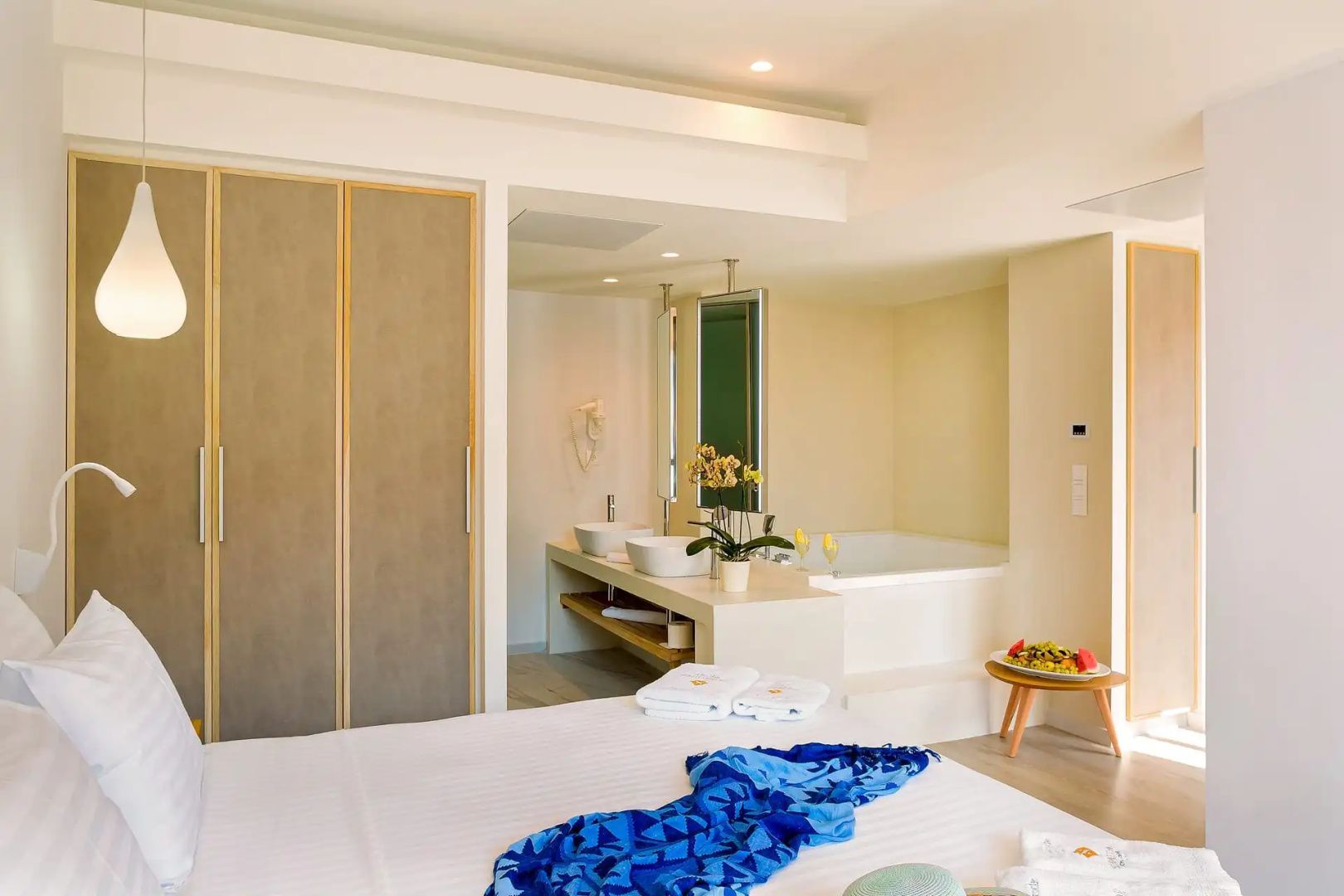 Offene Hotel Suite mit Doppelbett im Vordergrund und Badezimmer mit Doppelwaschbecken und Badewanne.