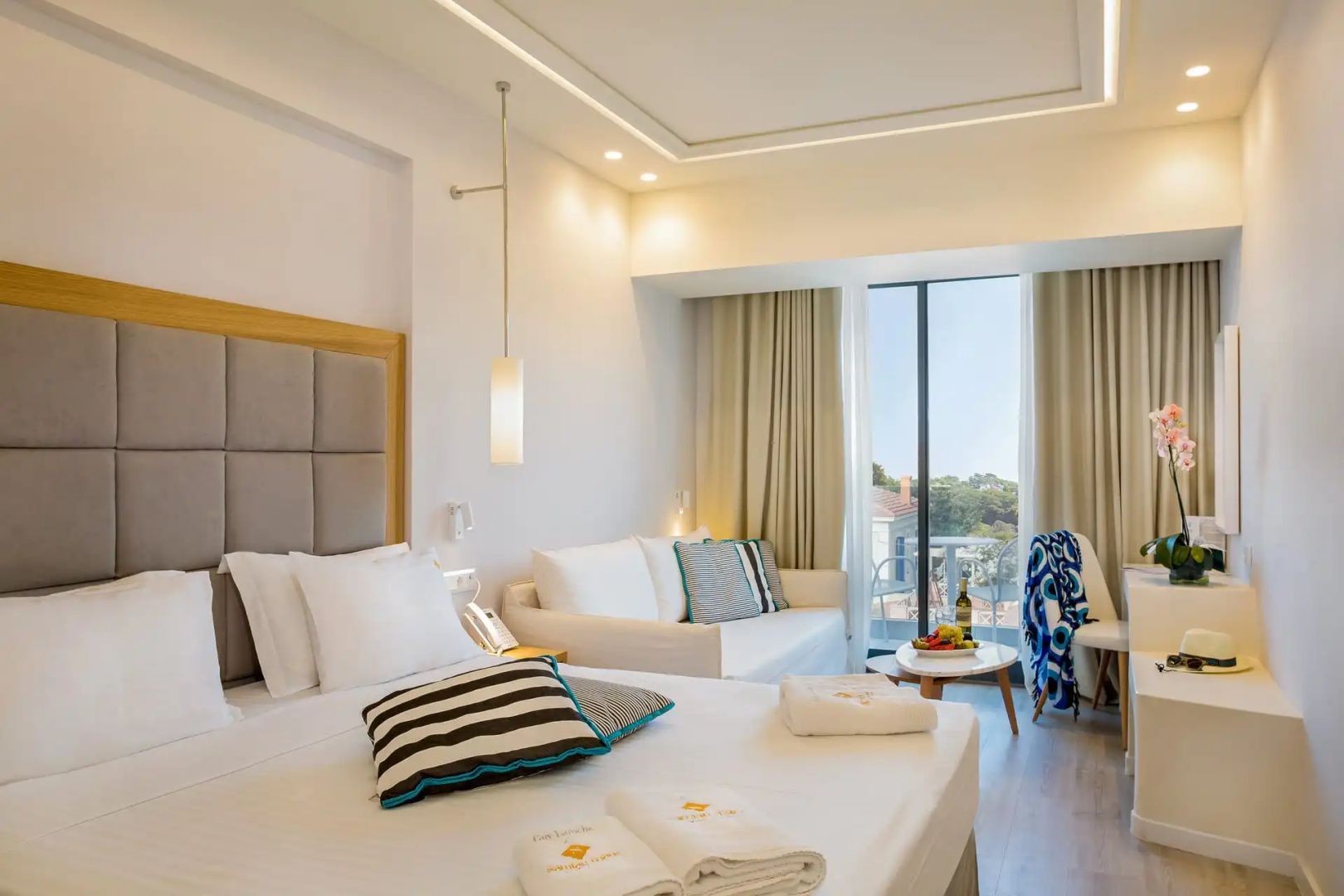 Ein helles Zimmer mit einem Doppelbett, weißem Sofa und Zugang zum Balkon.