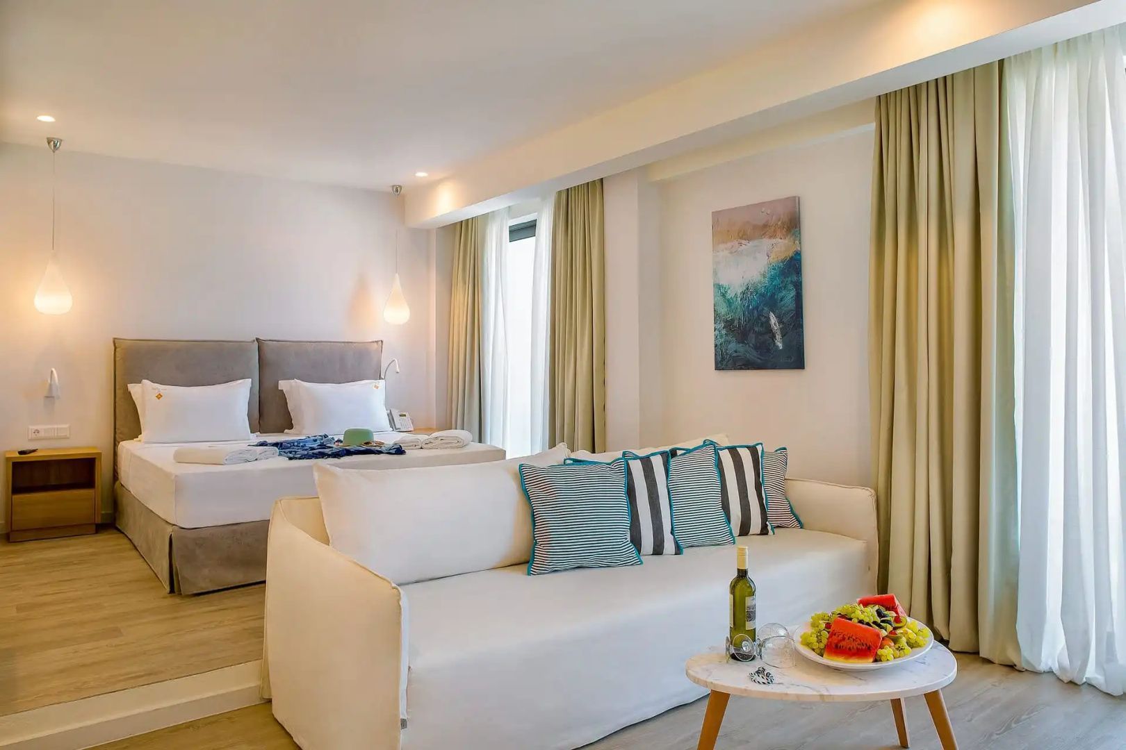Modern eingerichteter Wohnbereich einer Suite mit hellem Sofa, Couchtisch und Doppelbett im Hintergrund.
