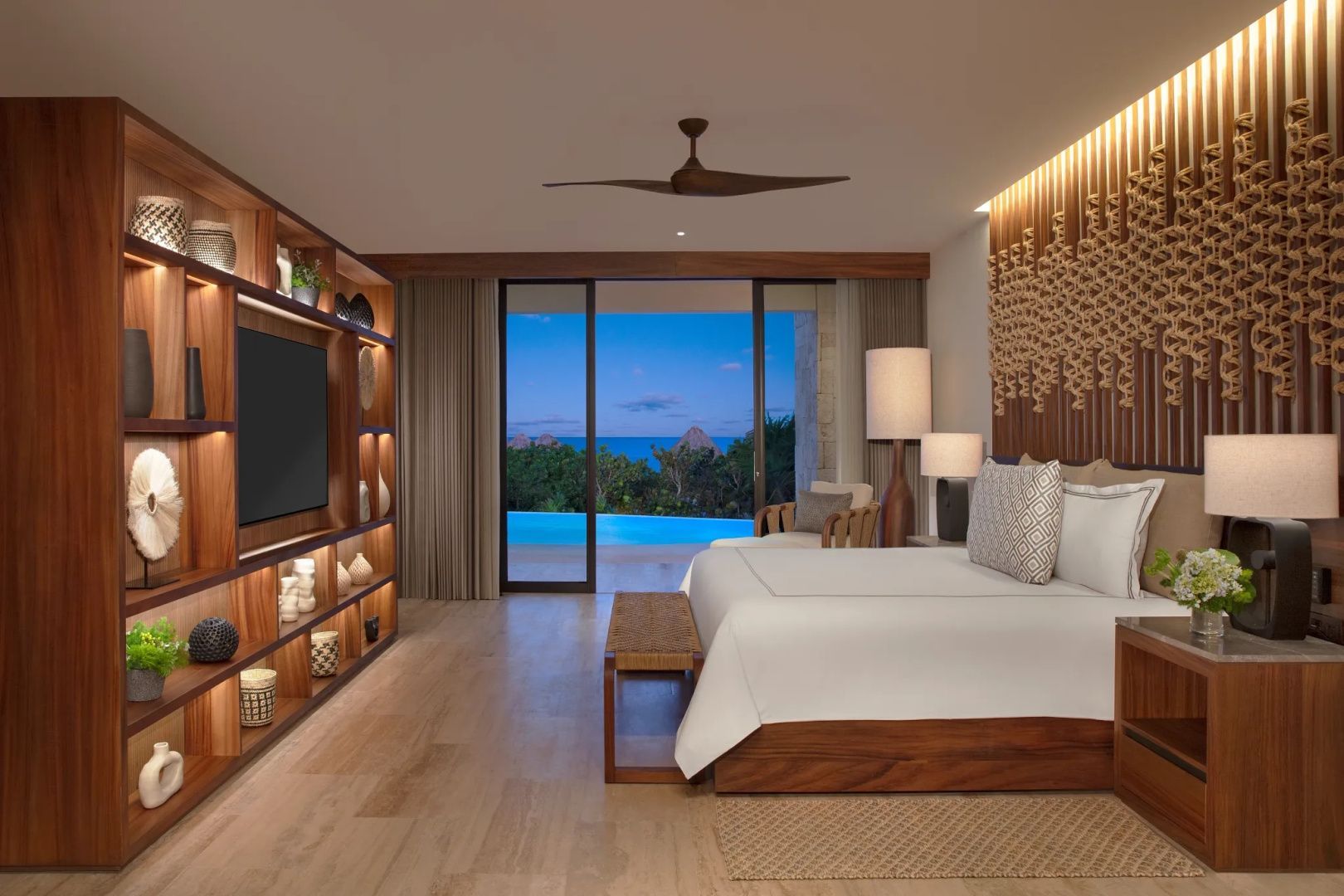 Schlafbereich mit Doppelbett, Fernseher im Holzregal und Blick auf die Terrasse mit Pool.