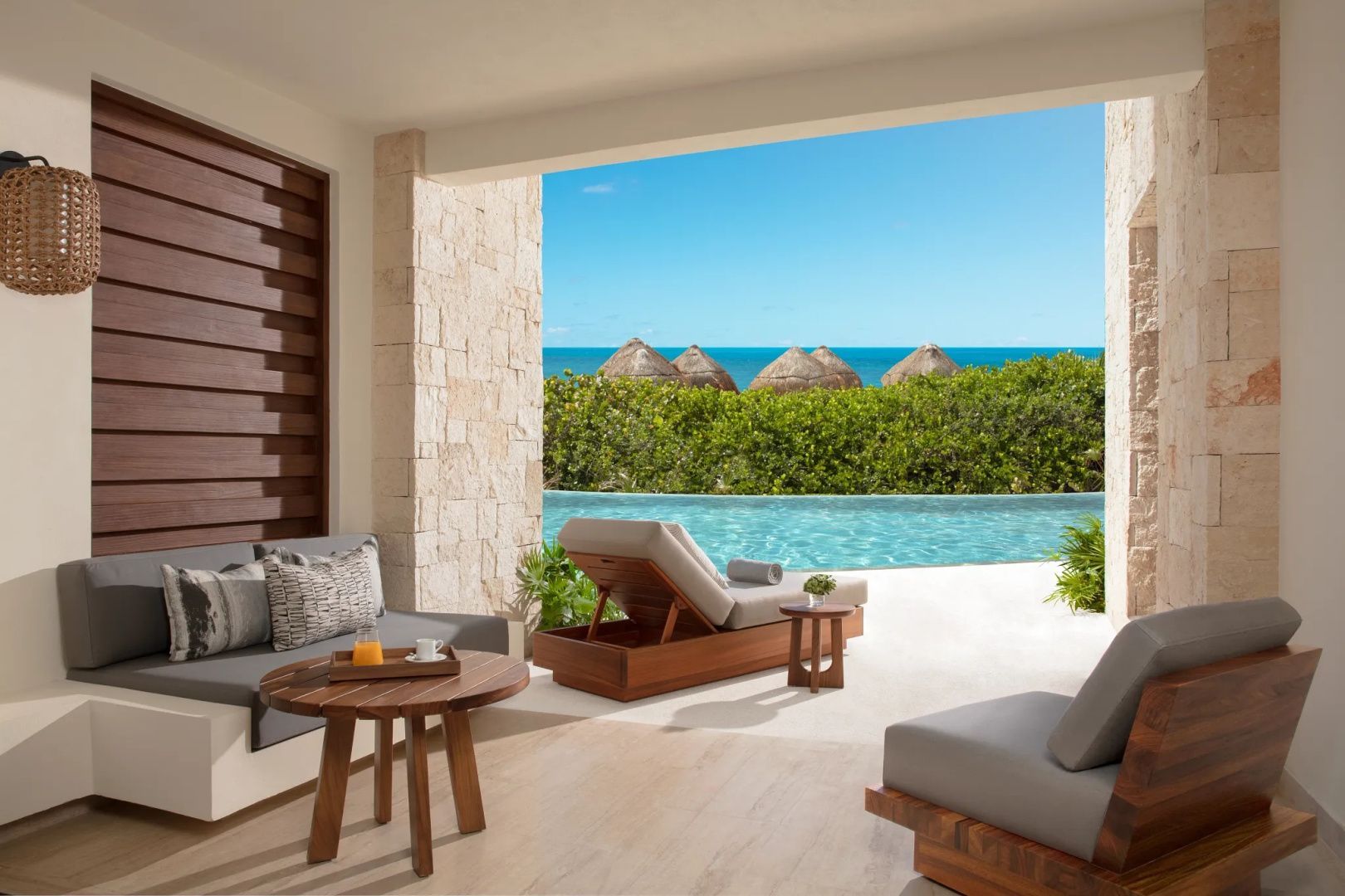 Überdachte Terrasse mit Holzmöbeln und Blick auf den Pool und das Meer.