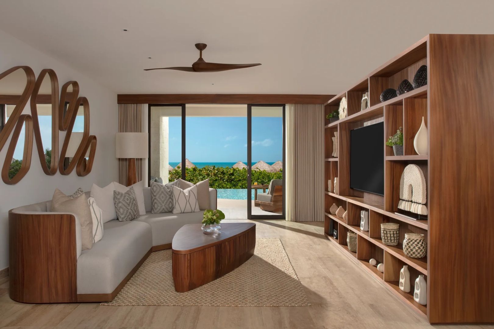 Wohnbereich einer Suite mit Ecksofa, Holzregal und Ausblick auf Terrasse und Meer.