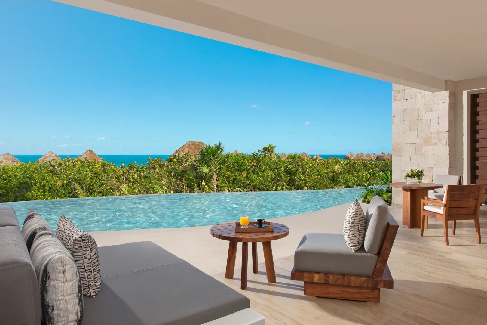 Terrasse mit Sitzmöbeln und Blick über den Infinitypool auf das blaue Meer.