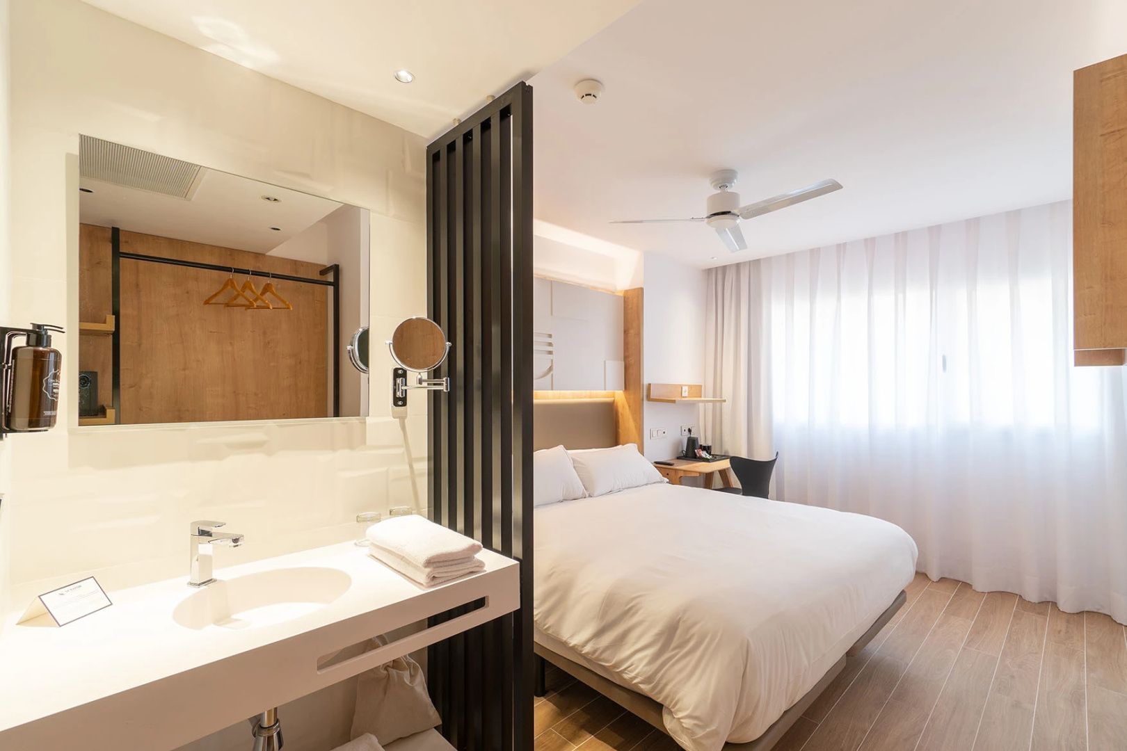 Modernes Hotelzimmer mit Doppelbett, Raumteiler und angrenzendem Waschtisch mit Spiegel.
