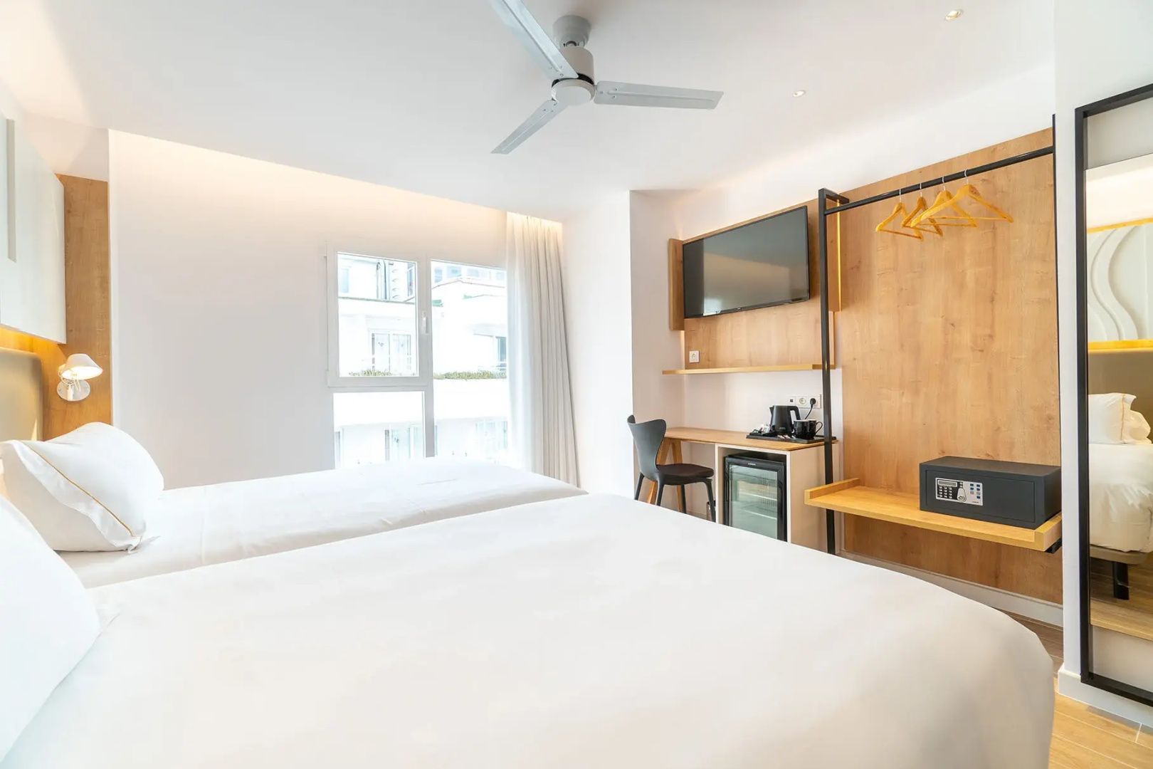 Blick vom Doppelbett auf den Schreibtisch mit Wand TV und ein großes Fenster zum Balkon.