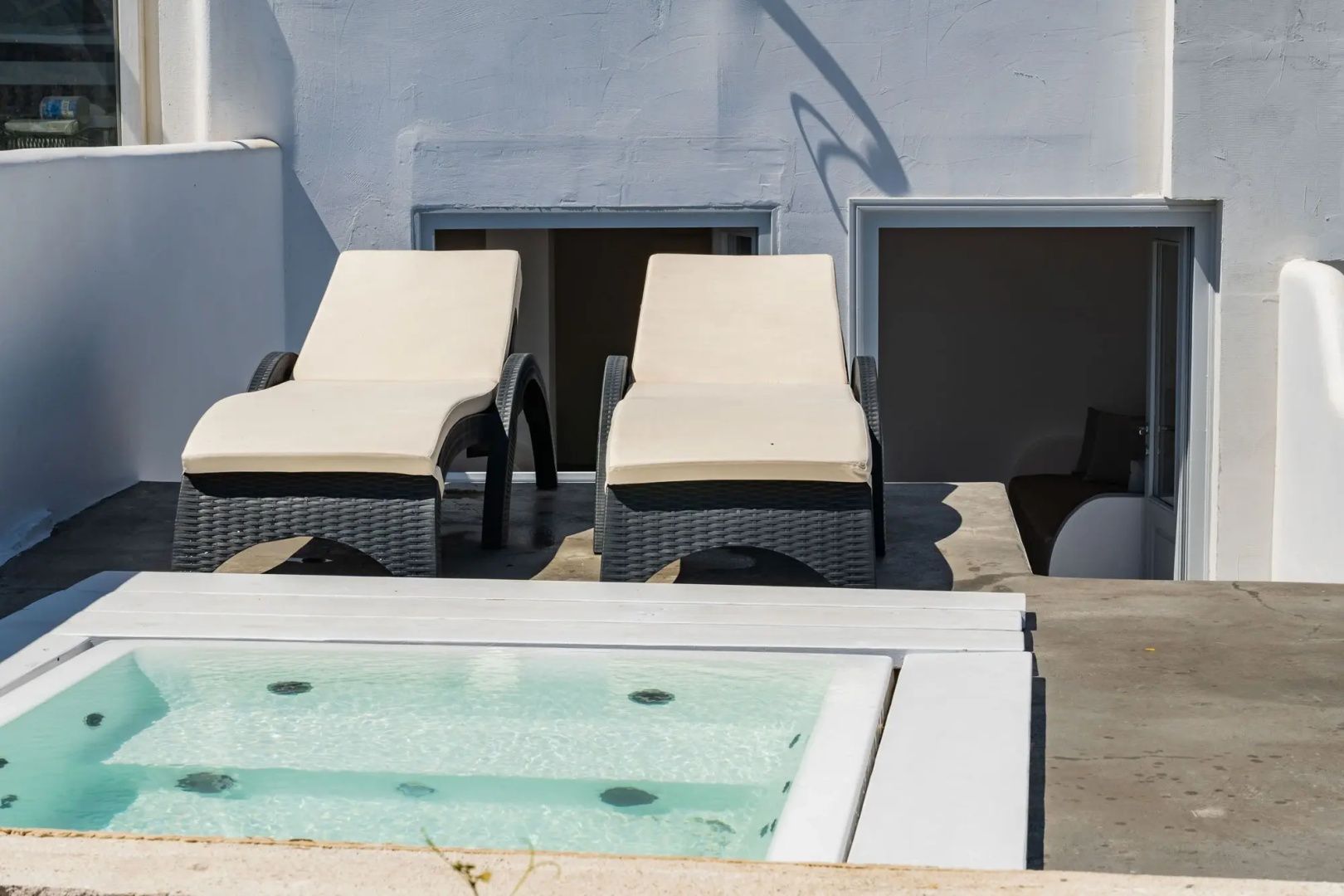 Zwei Sonnenliegen mit hellen Auflagen stehen neben einem kleinen Pool auf einer weißen Terrasse.