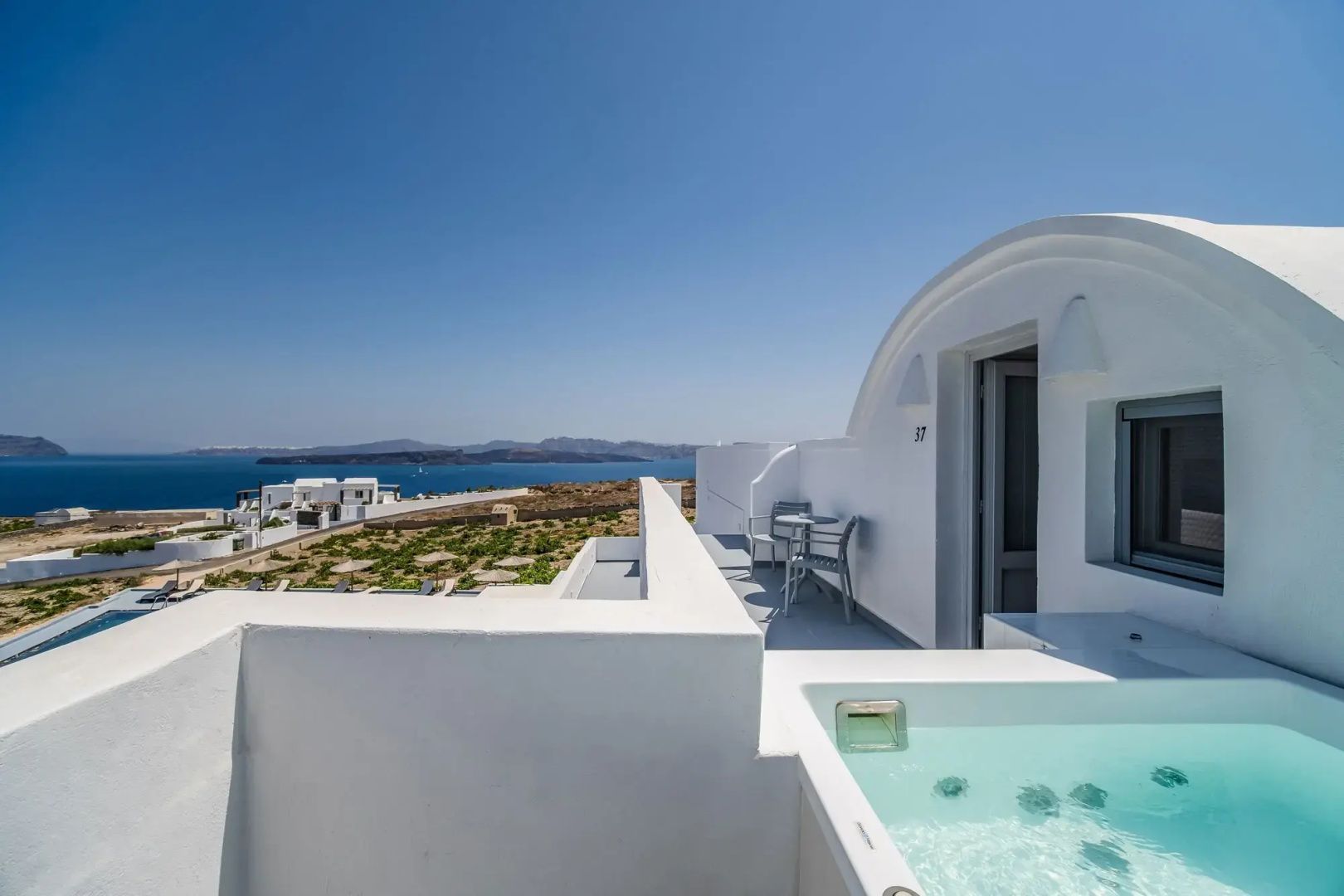 Sonnige Terrasse einer weißen Suite mit Whirlpool, Sitzbereich und Blick auf das Meer.