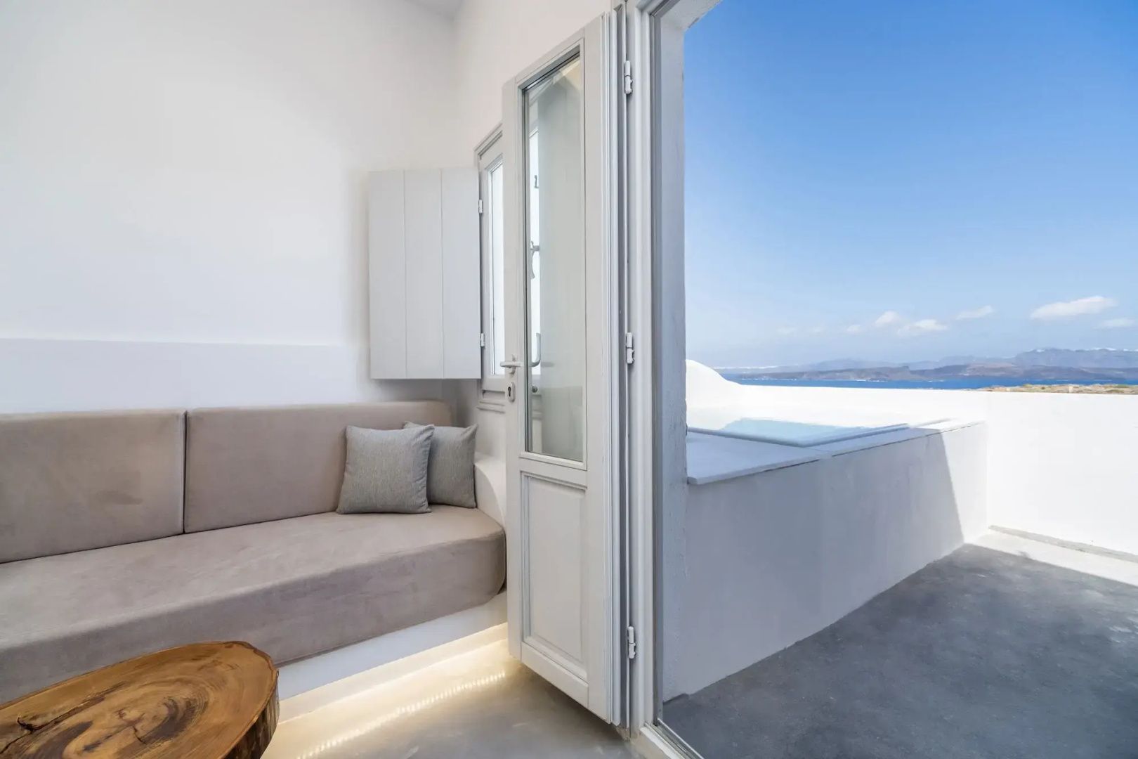 Helles Zimmer mit Sitzbank und geöffneter Balkontür mit Blick auf Terrasse und Meer.