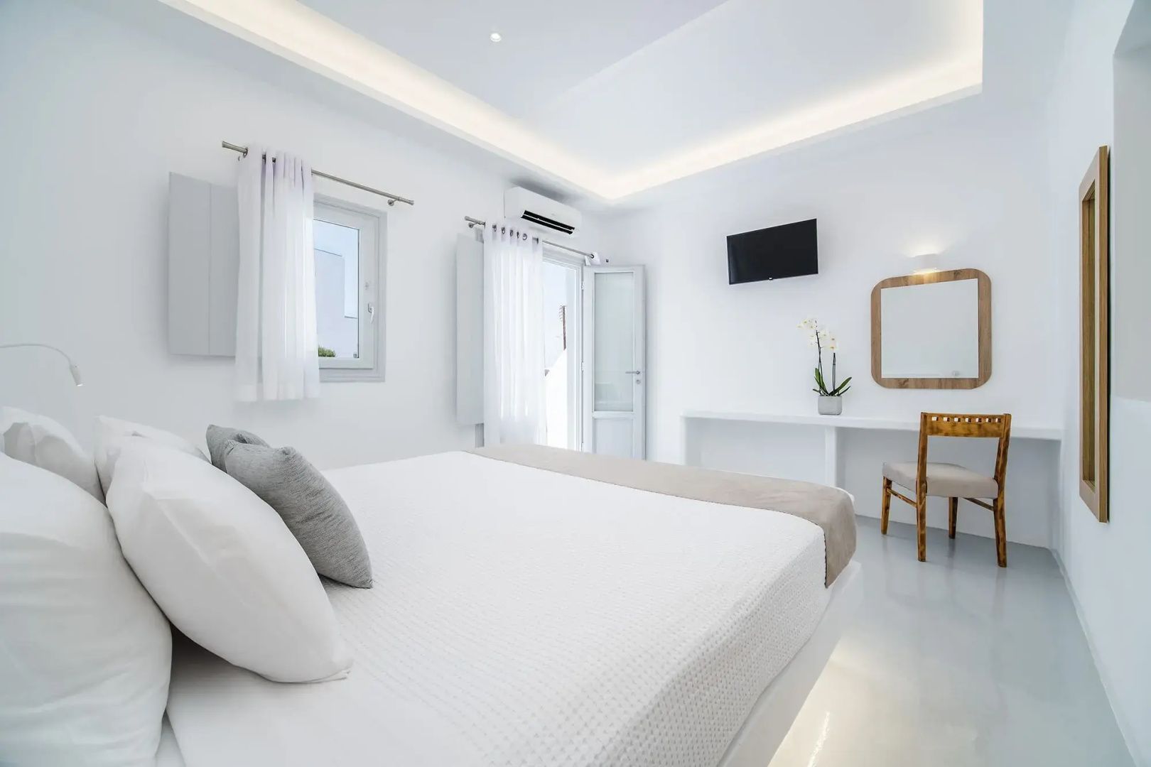Schlafzimmer in Weiß mit Schreibtisch, Wand-TV und einem Holzstuhl.