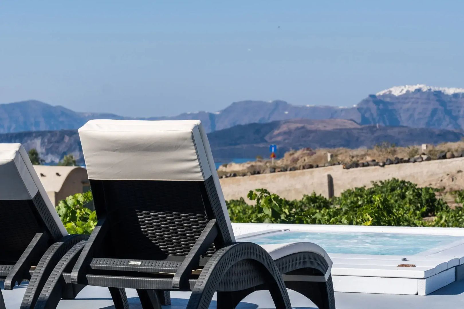 Liegestuhl auf einer Terrasse mit Blick auf eine felsige Hügellandschaft und blaues Meer.