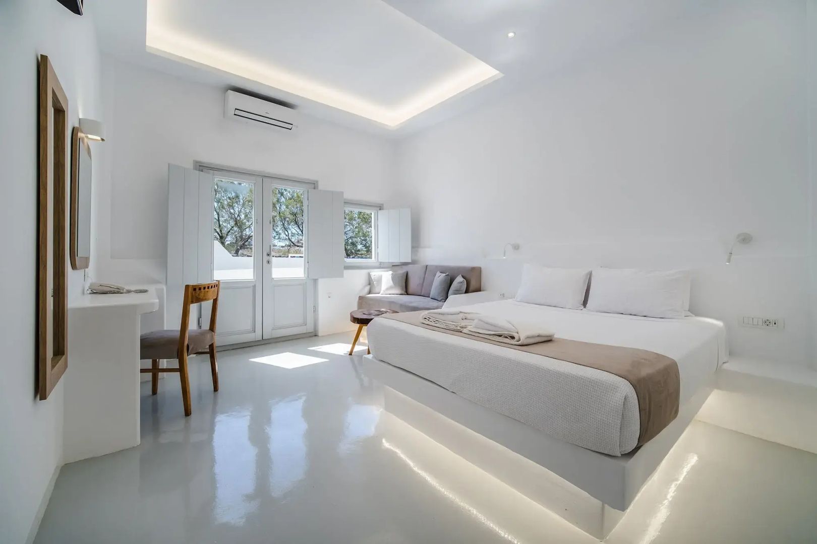 Schlafzimmer mit weißem Doppelbett, Sofa und Tür zur Terrasse.