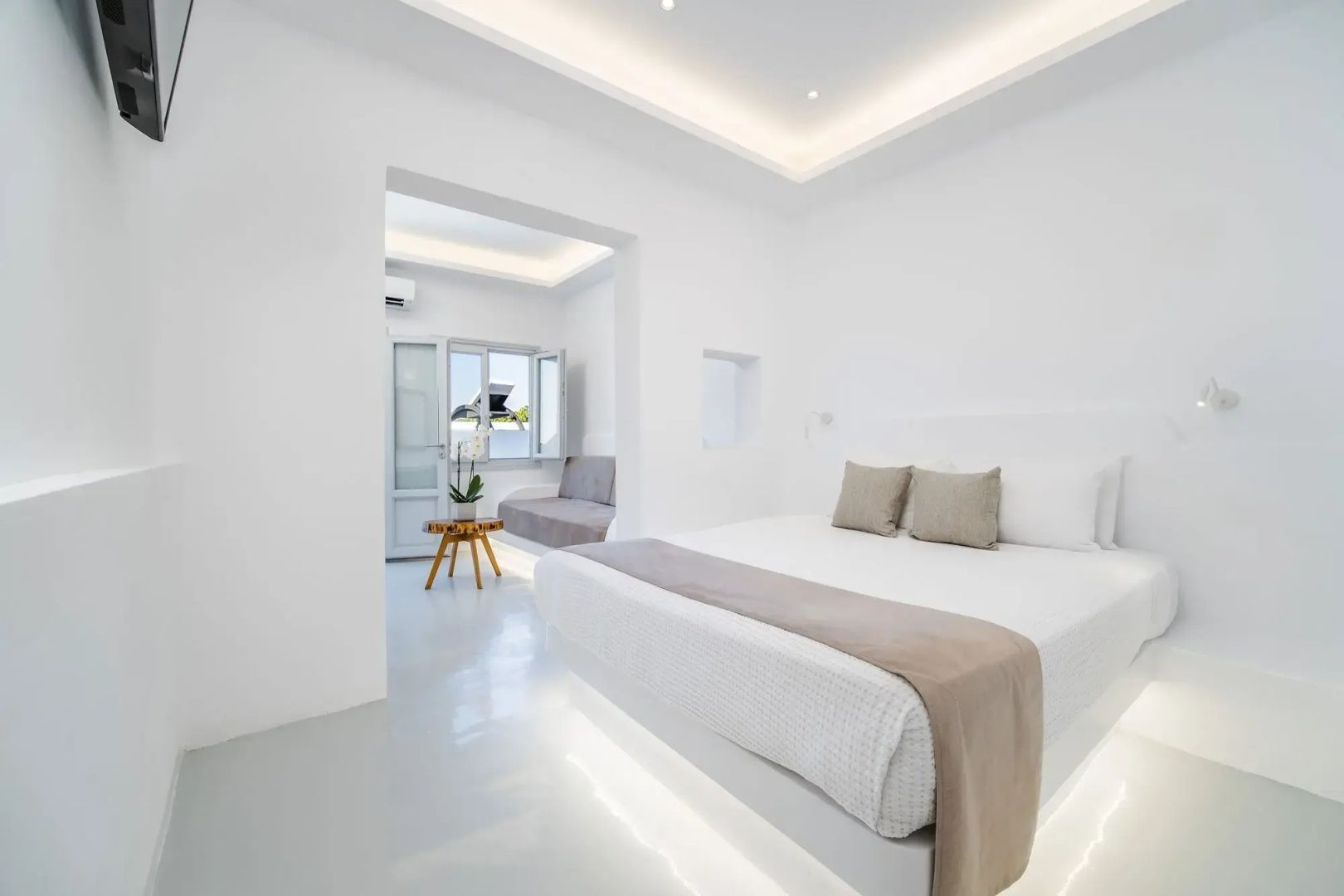Weiß eingerichtetes Hotelzimmer mit großem Doppelbett und Durchgang zu einem Sitzbereich.