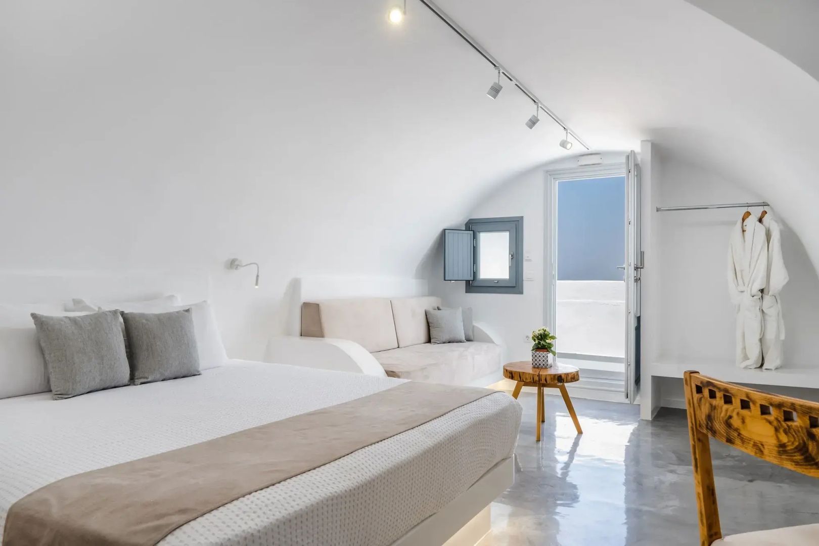 Weißes Schlafzimmer mit Gewölbedecke, beige Couch und kleinem Holztisch sowie Blick zur Tür.